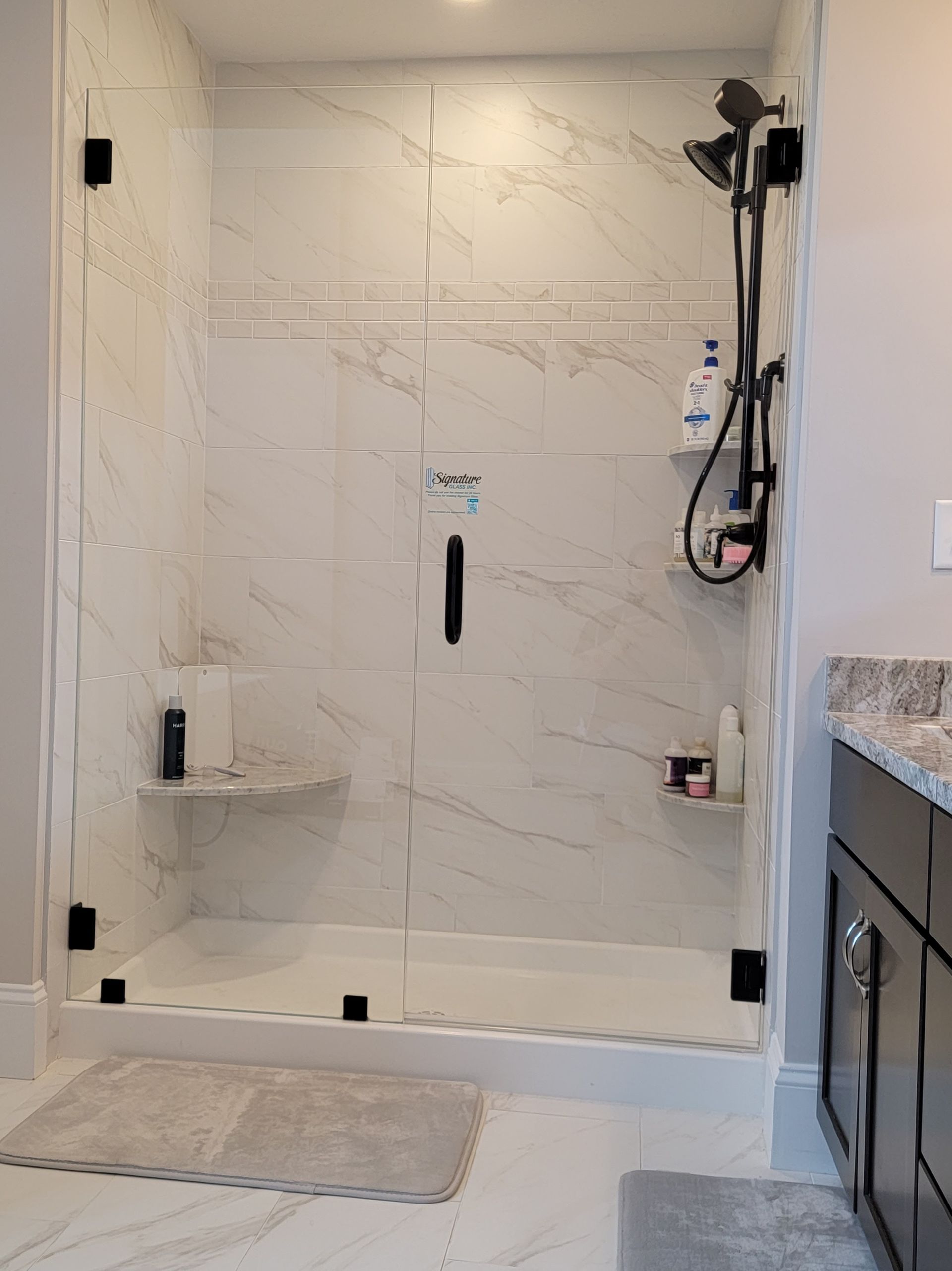 Modern shower with marble-look tile, glass doors, and black fixtures.