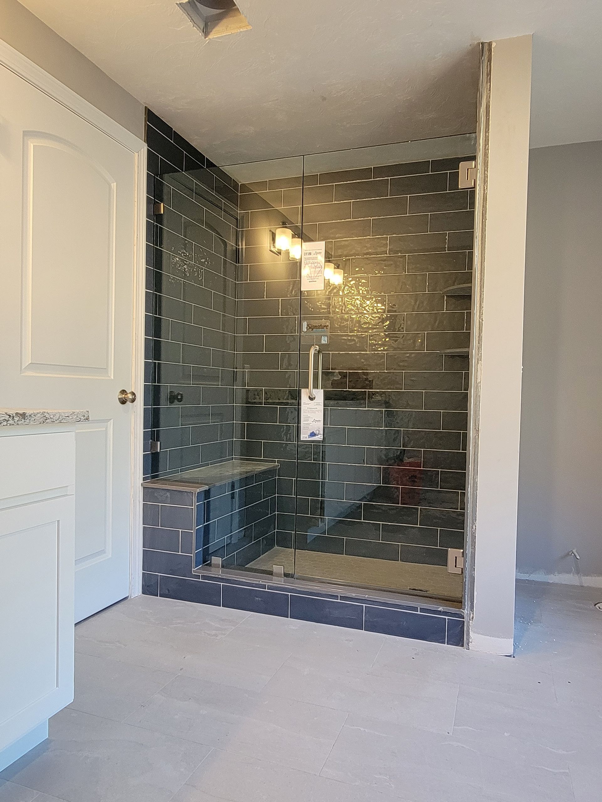 Newly constructed shower with glass door and dark gray tile.