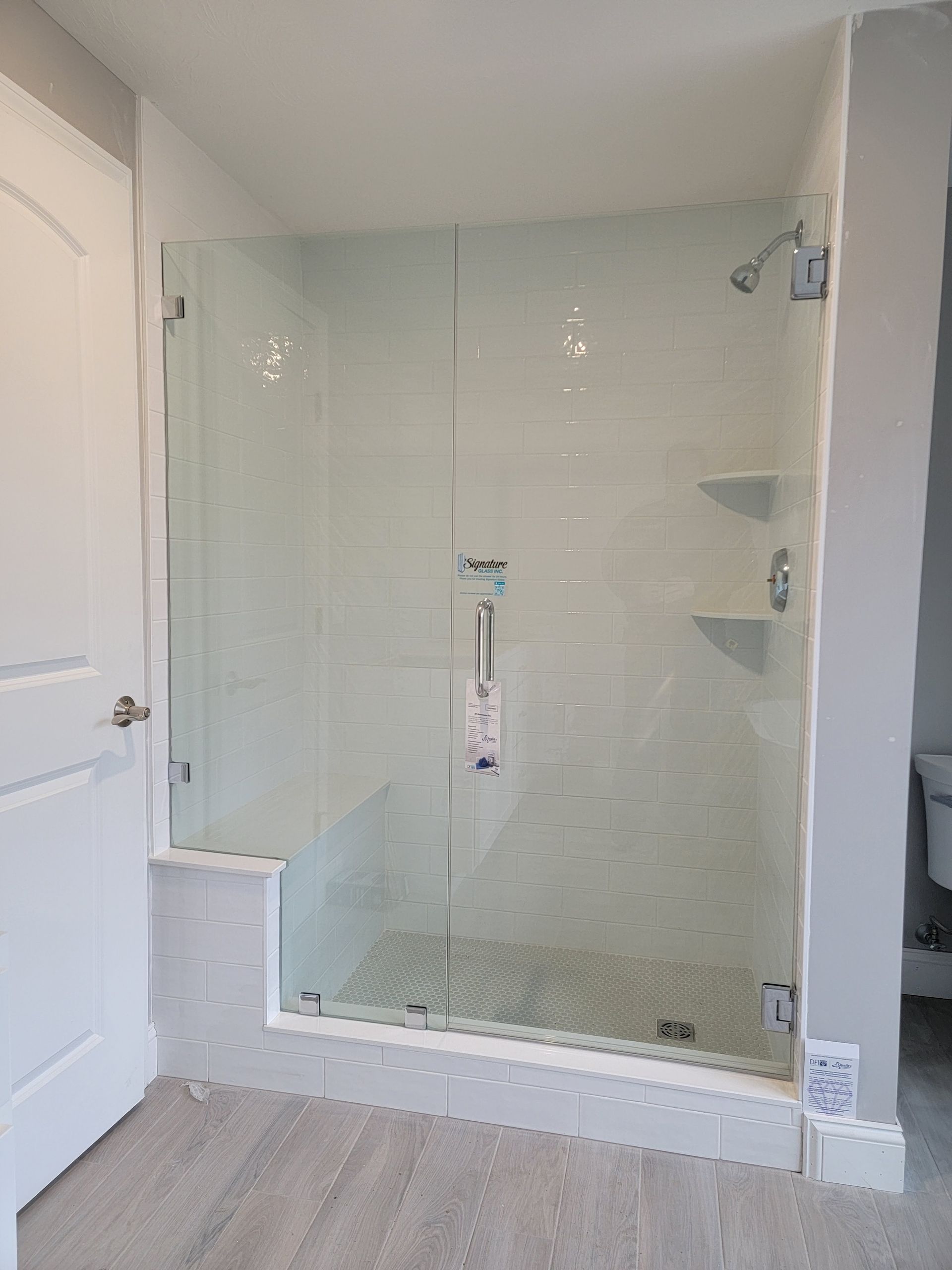 Glass shower enclosure with white tile and chrome fixtures.