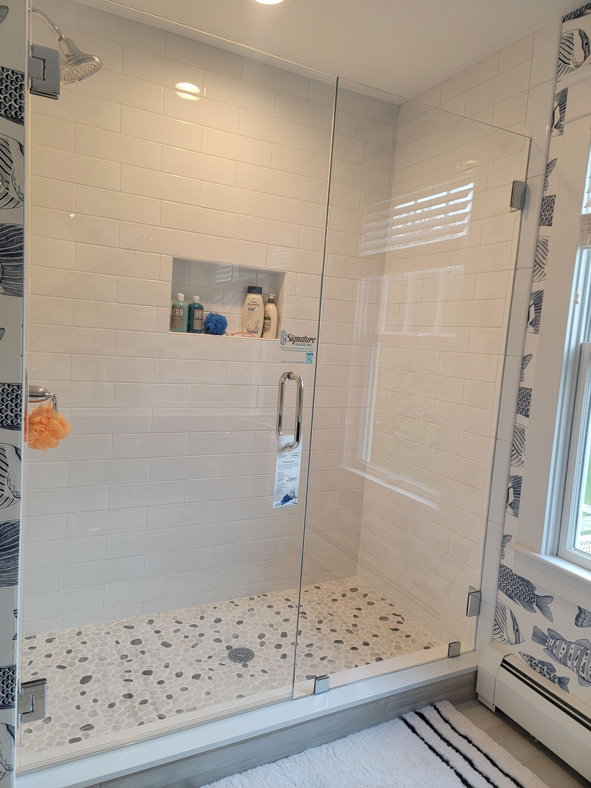 A modern bathroom shower with a glass door, white tiles, and pebble floor.