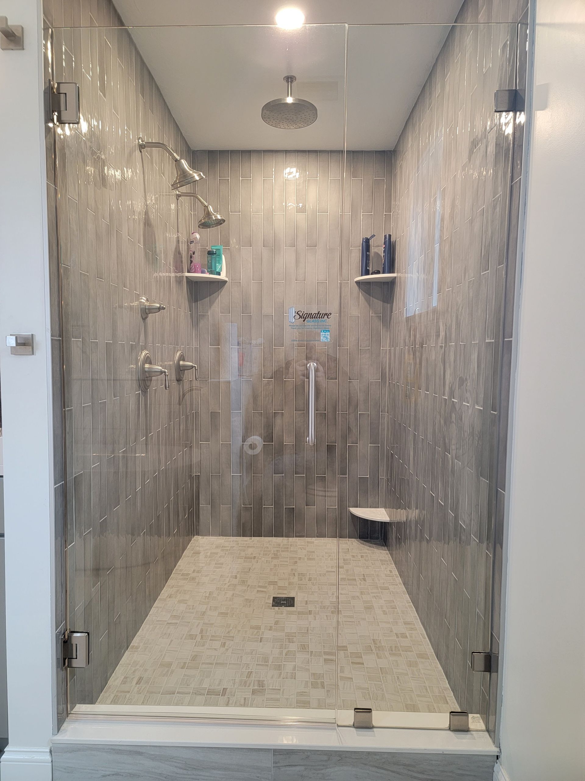 Modern shower stall with gray tiled walls, glass doors, and multiple showerheads.