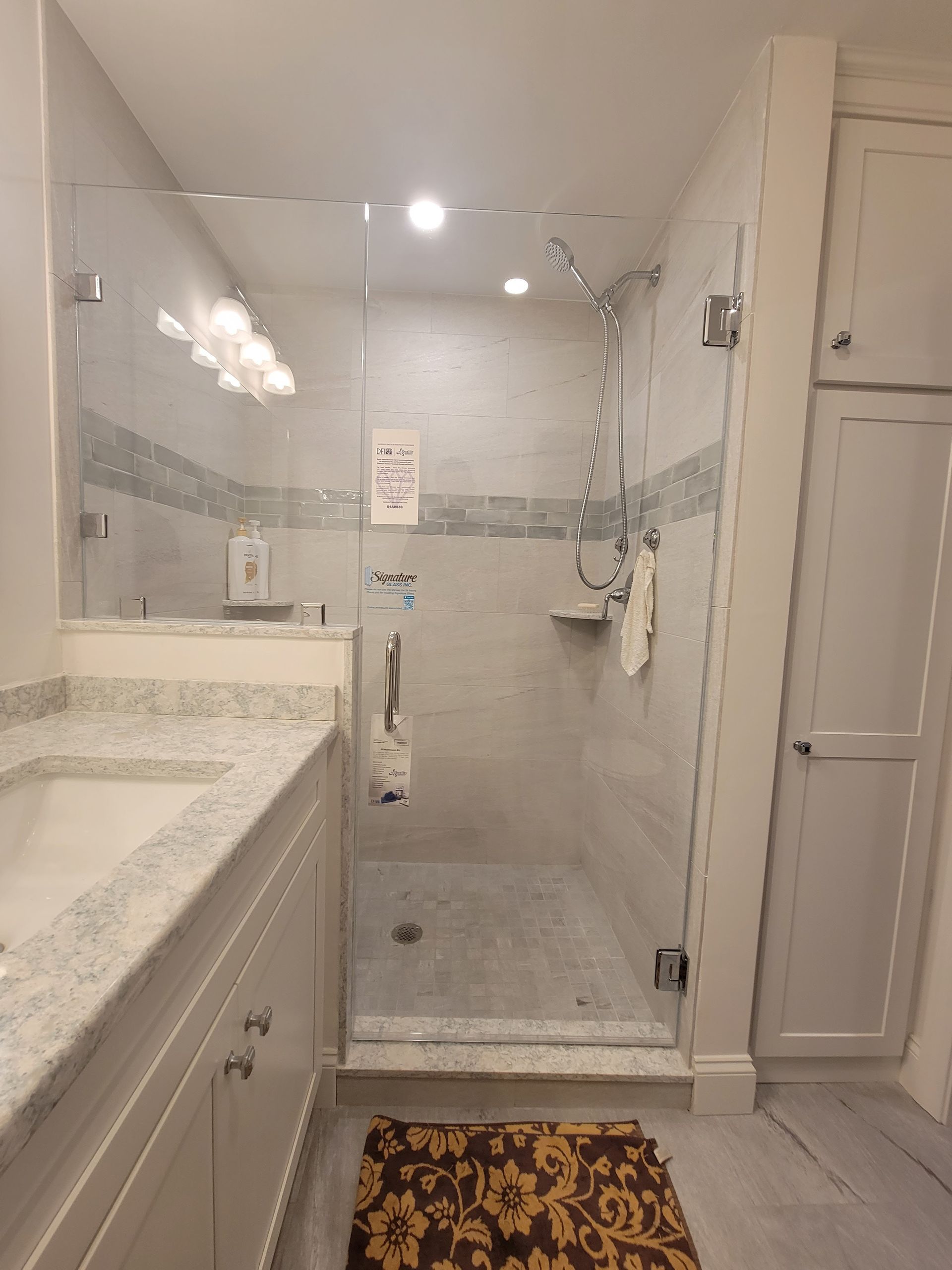Bathroom with a glass shower, white vanity, and patterned rug.