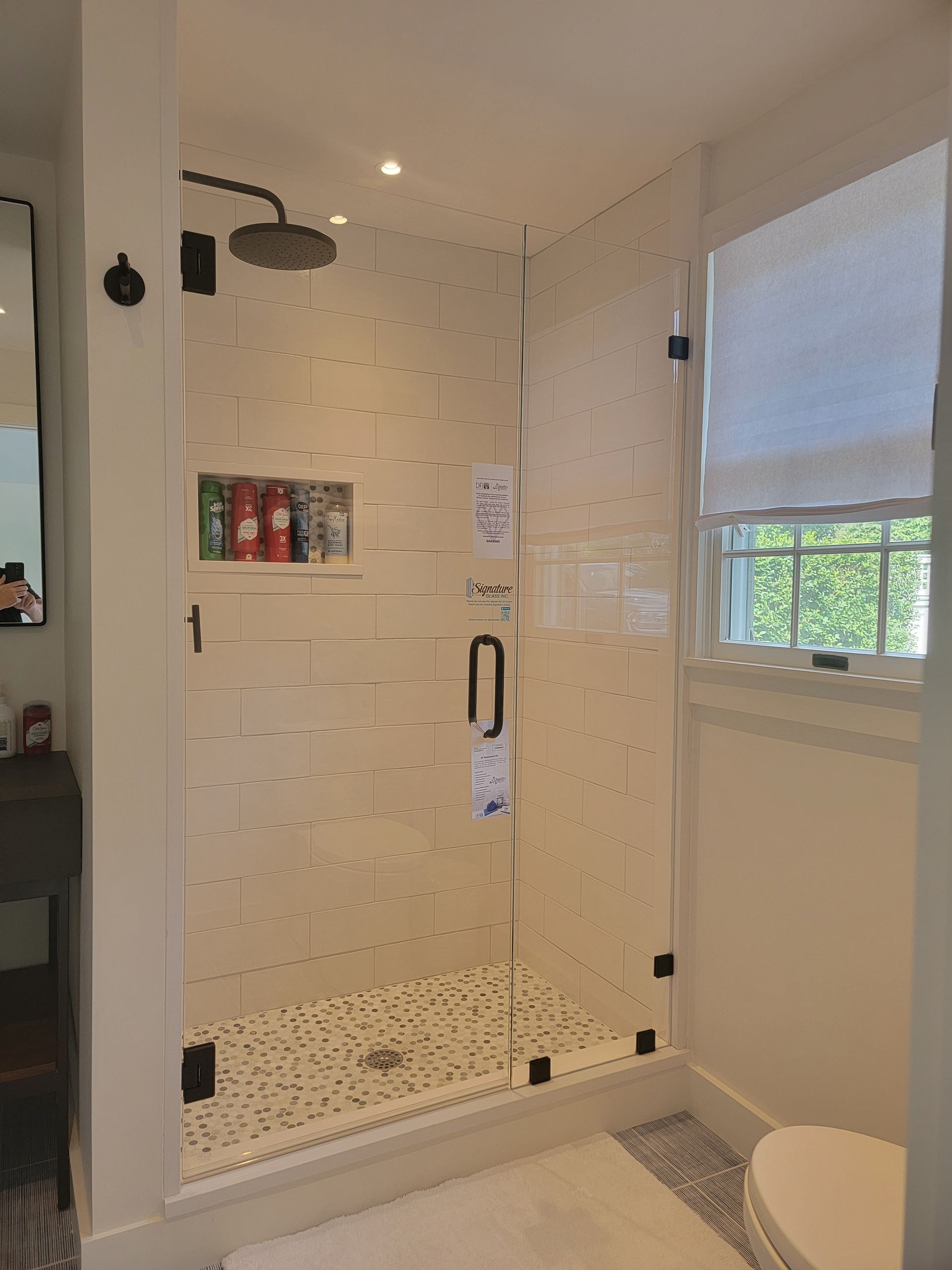 Modern bathroom with a glass shower enclosure, white tiles, and a small window.