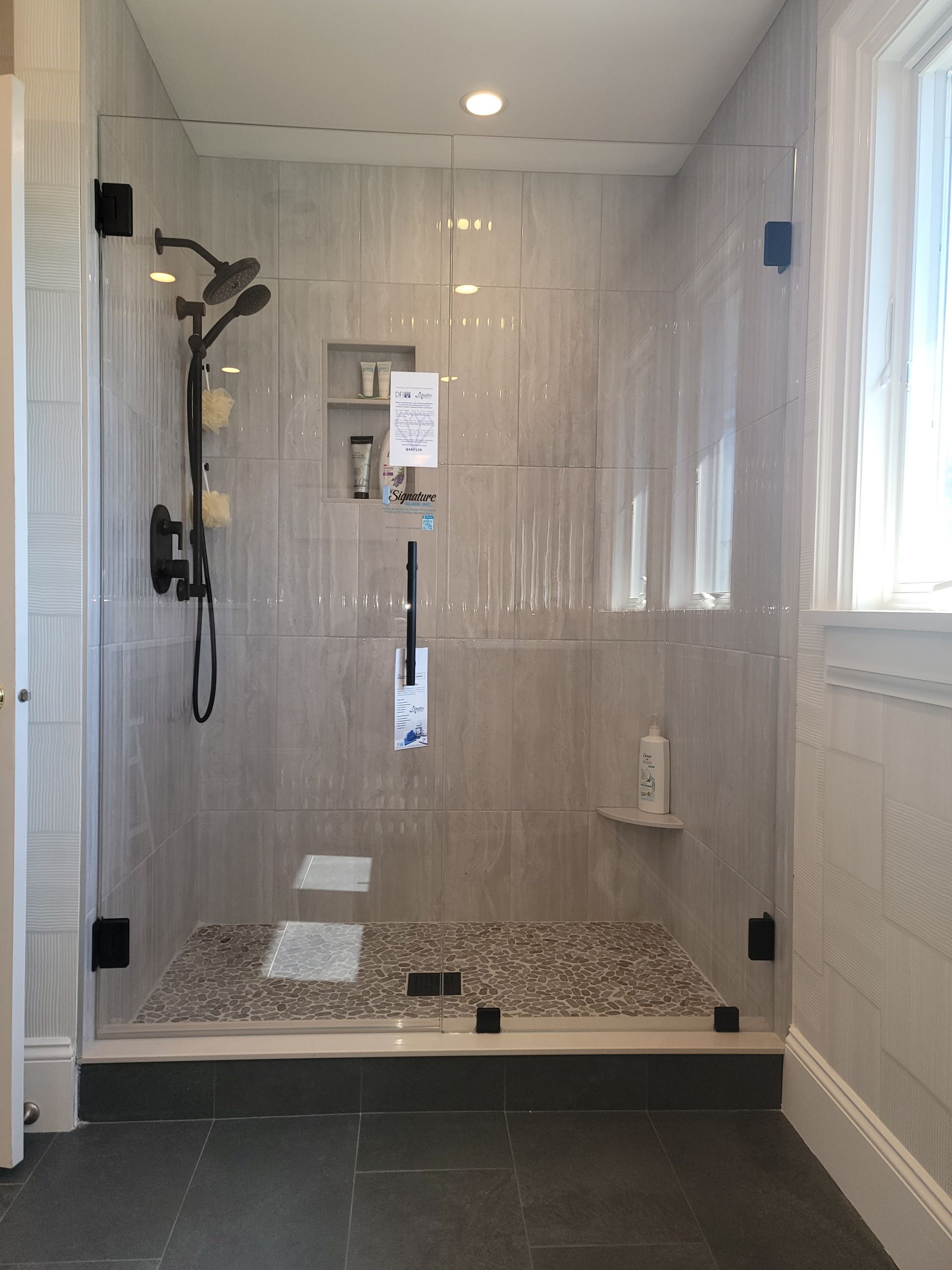 Glass shower with pebble floor, black fixtures, and built-in shelves.