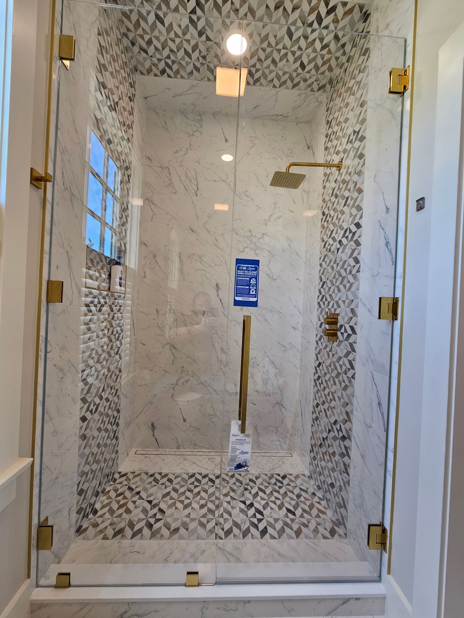 Glass shower with marble and mosaic tile, gold fixtures.