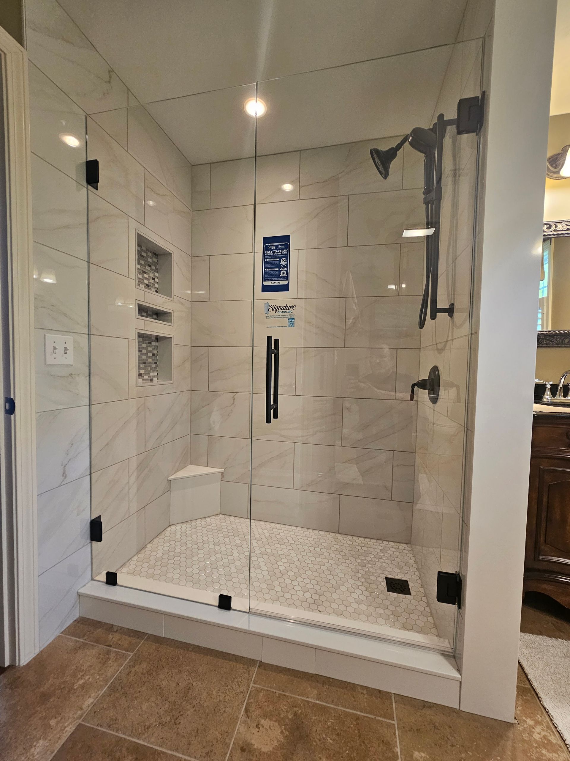 Glass-enclosed shower with white tiled walls, pebble floor, and black fixtures.