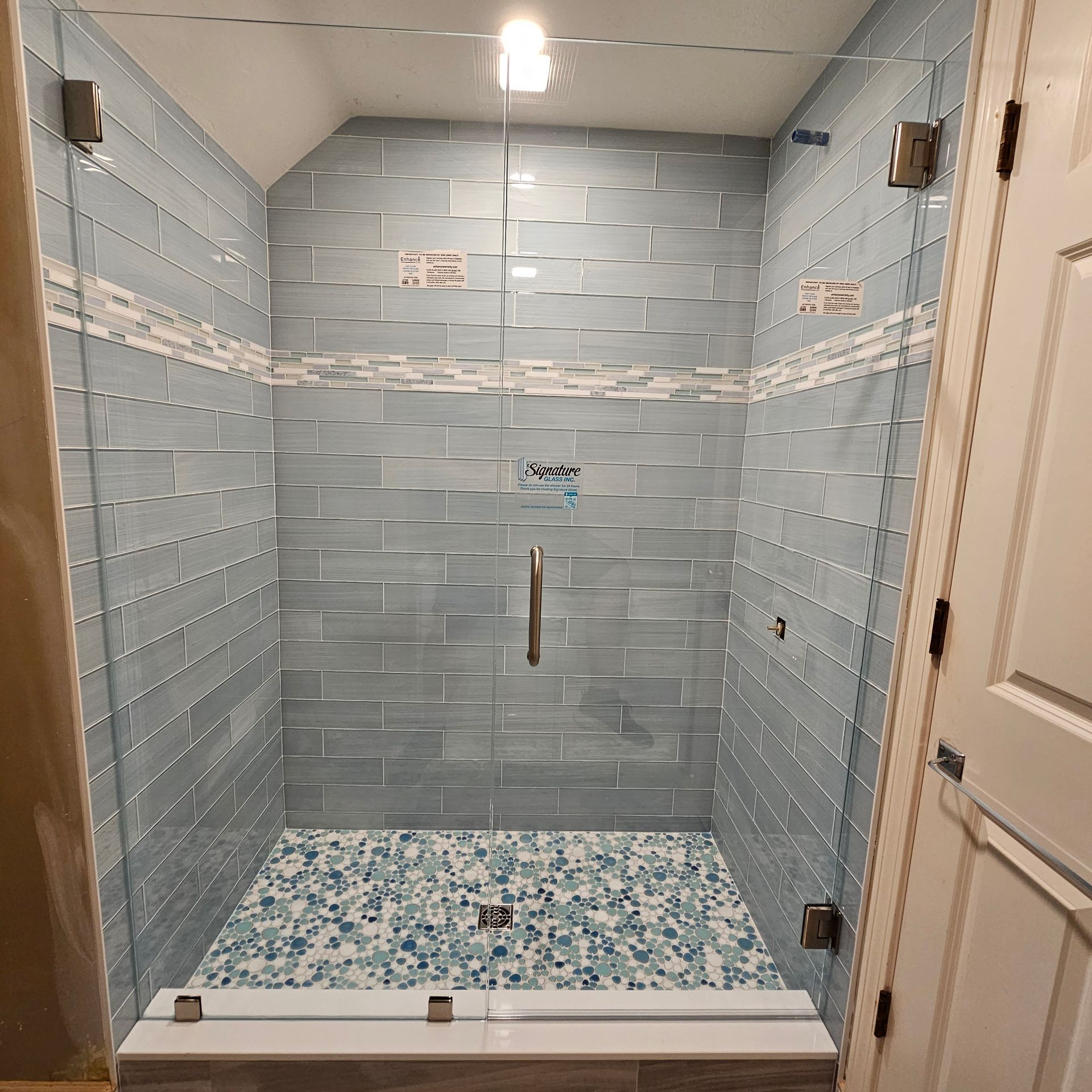 Shower with blue tile walls, glass doors, and pebble floor.