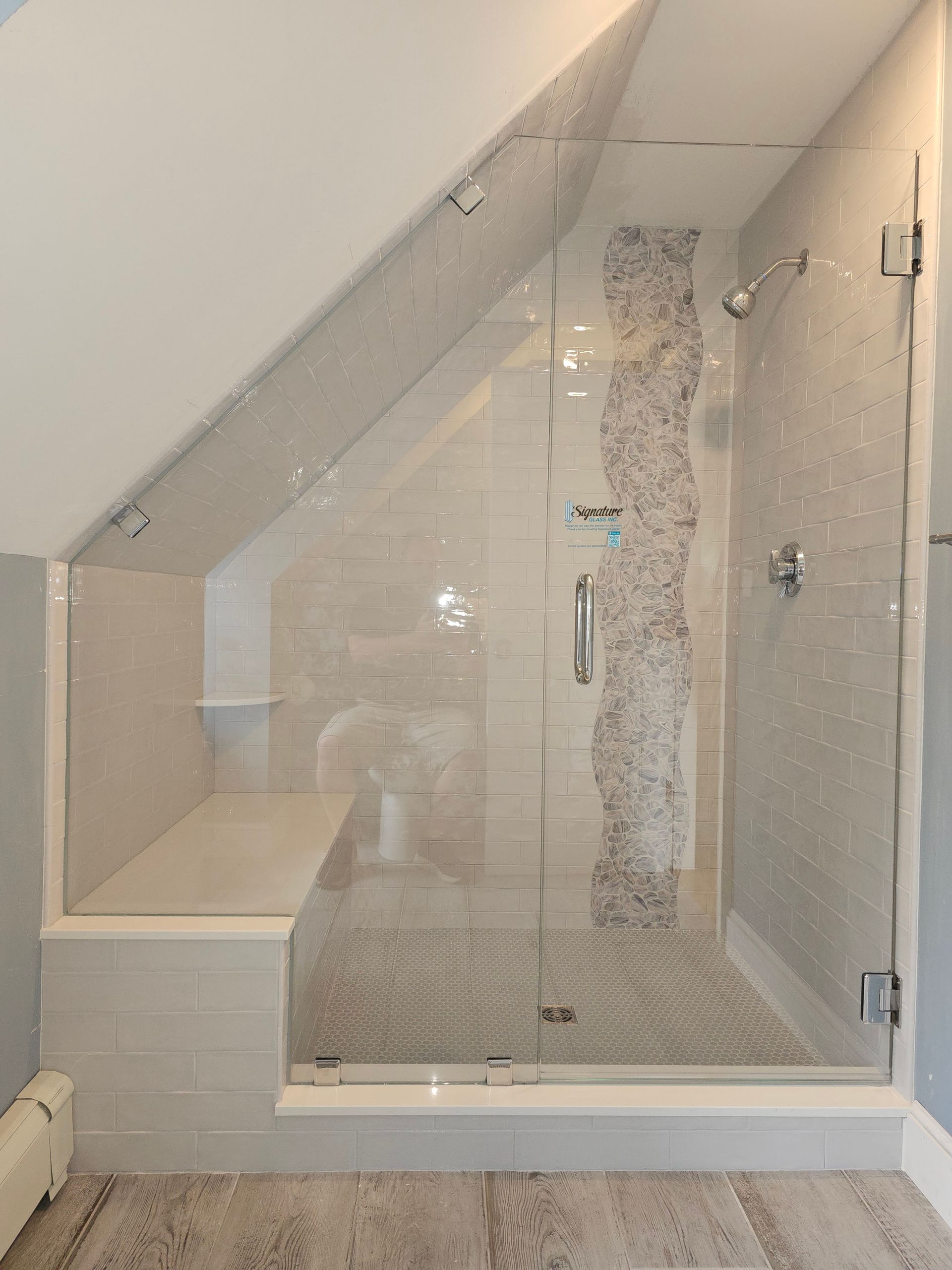 Modern shower with angled glass door and built-in bench in a bathroom with white and gray tiling.
