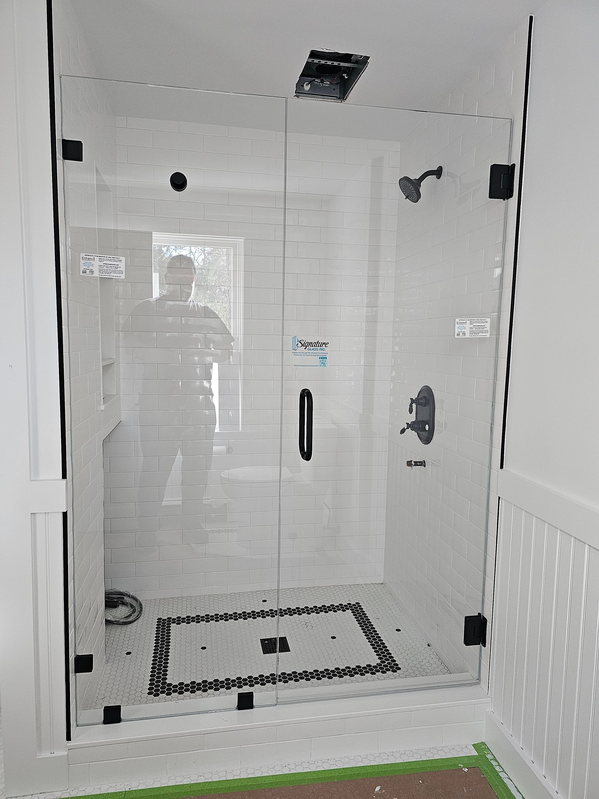 Glass shower with black hardware, white tile, and patterned floor.