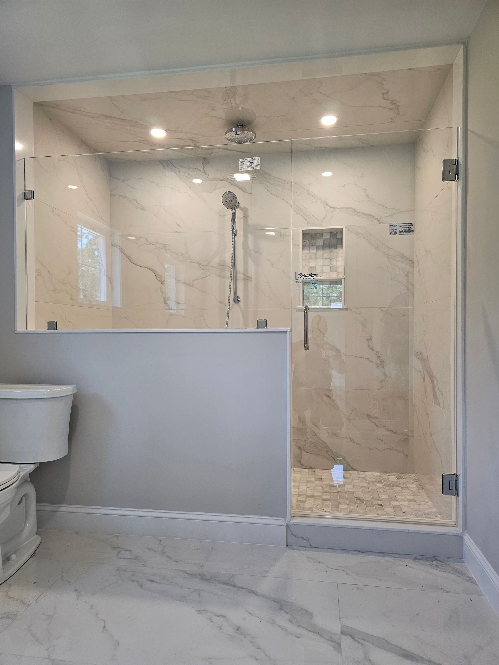 Modern walk-in shower with glass doors and marble tile walls, adjacent to a toilet.