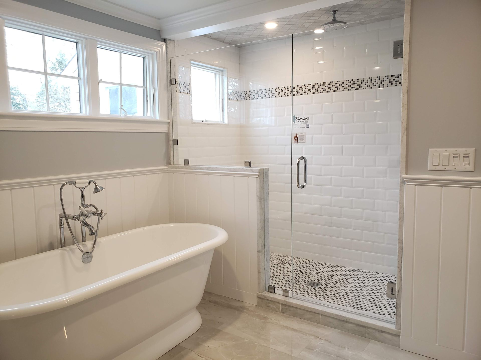 Bathroom with a white bathtub, glass shower, and white and gray tiled walls.