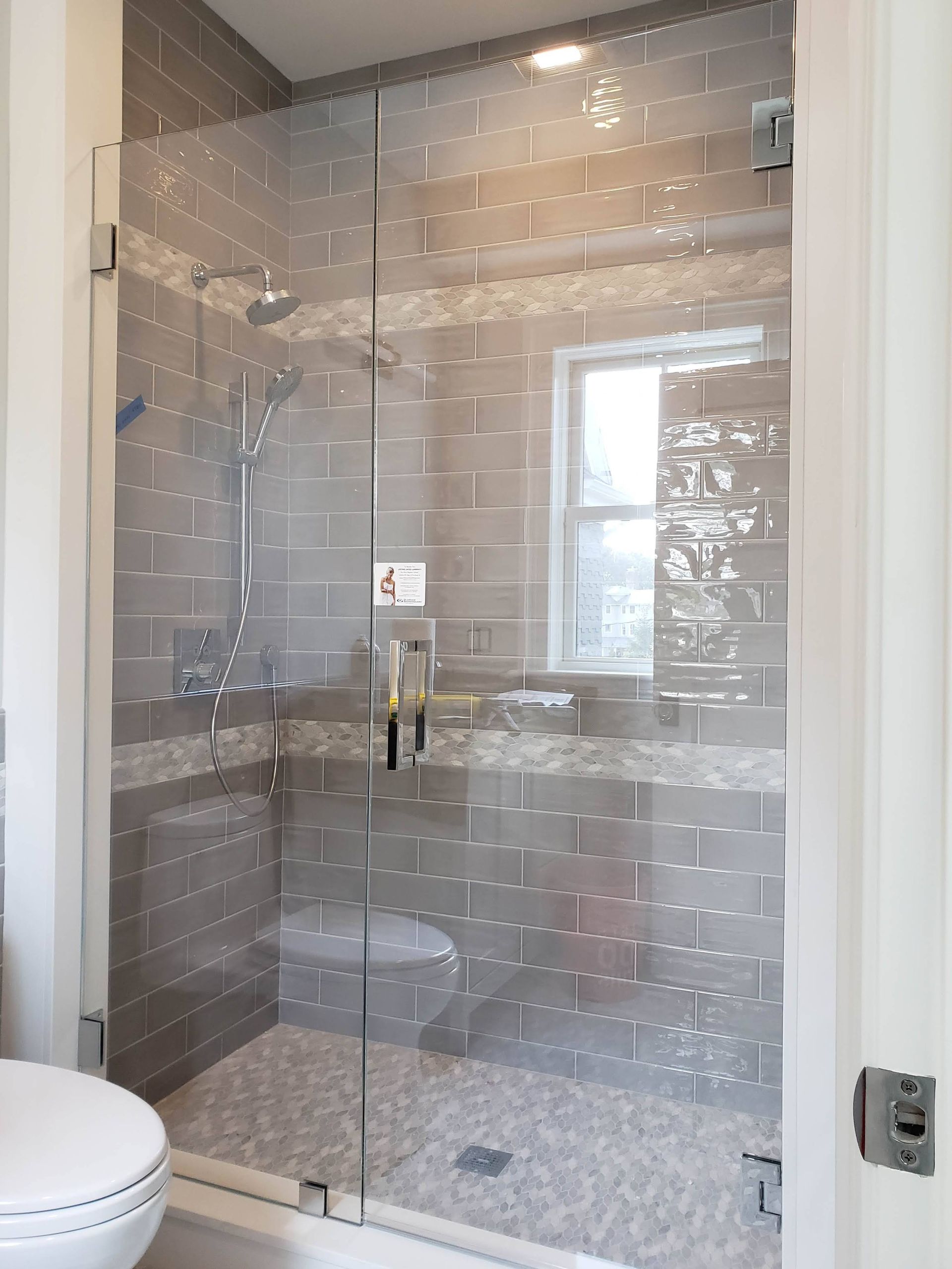 Glass shower with gray tile walls, pebble floor, and a small window.