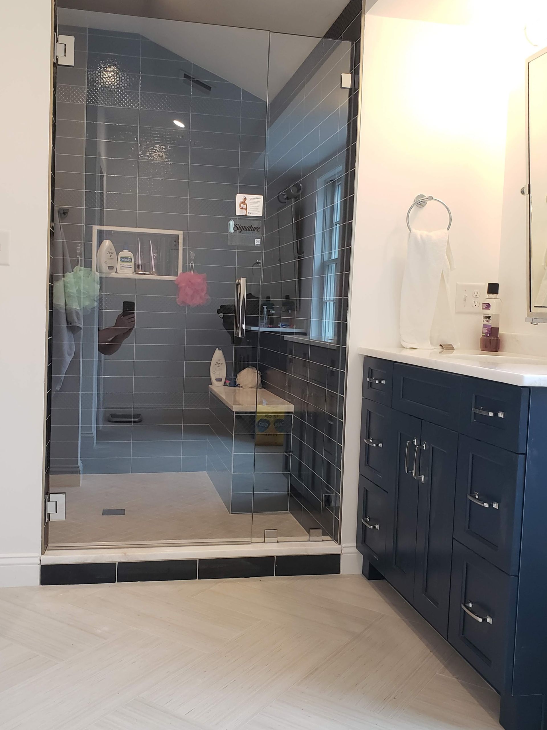 Bathroom with glass shower, navy vanity, white countertop, and gray tiled shower walls.