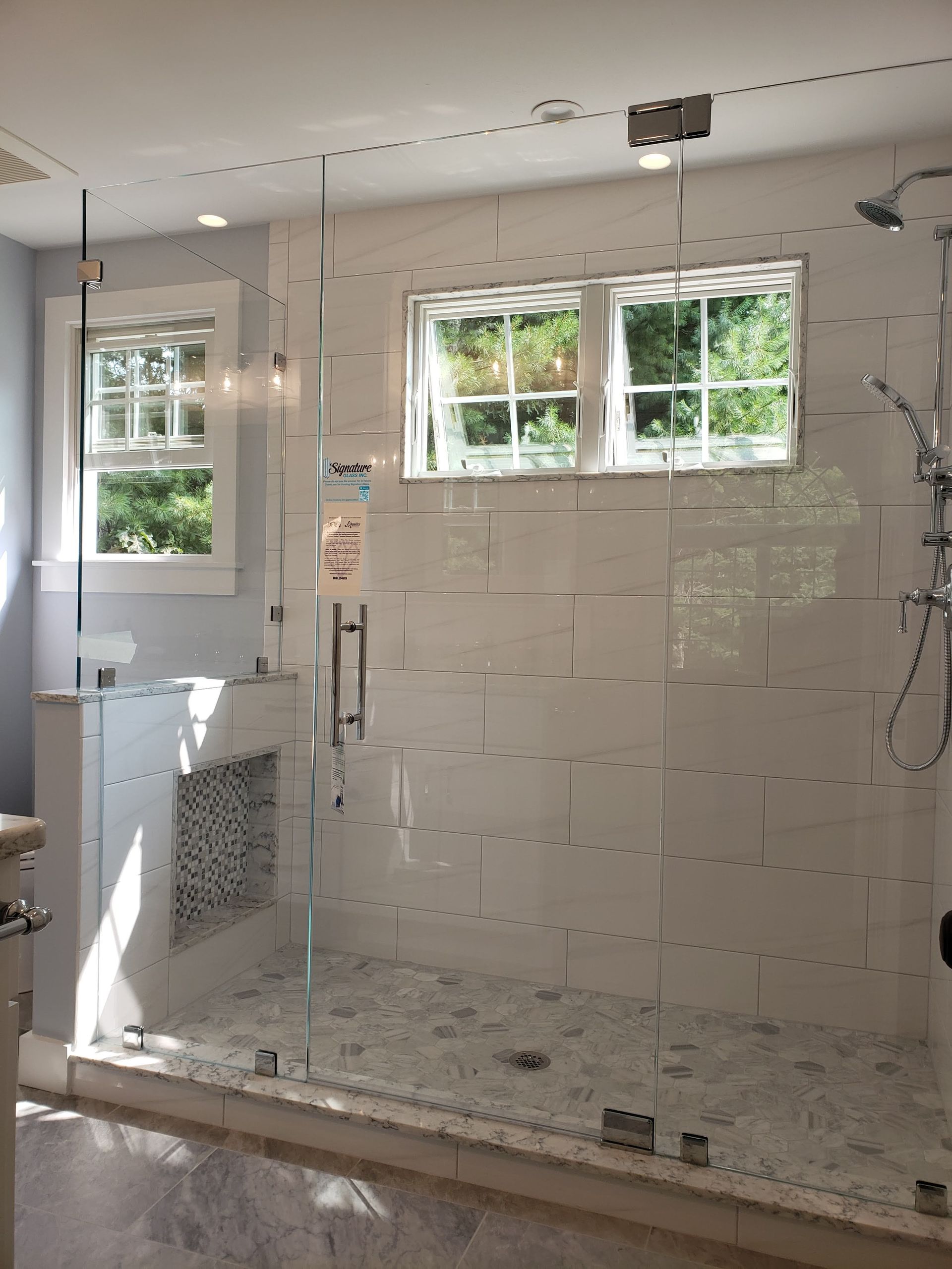 Bathroom with glass shower, white tile, two windows, and stone floor.