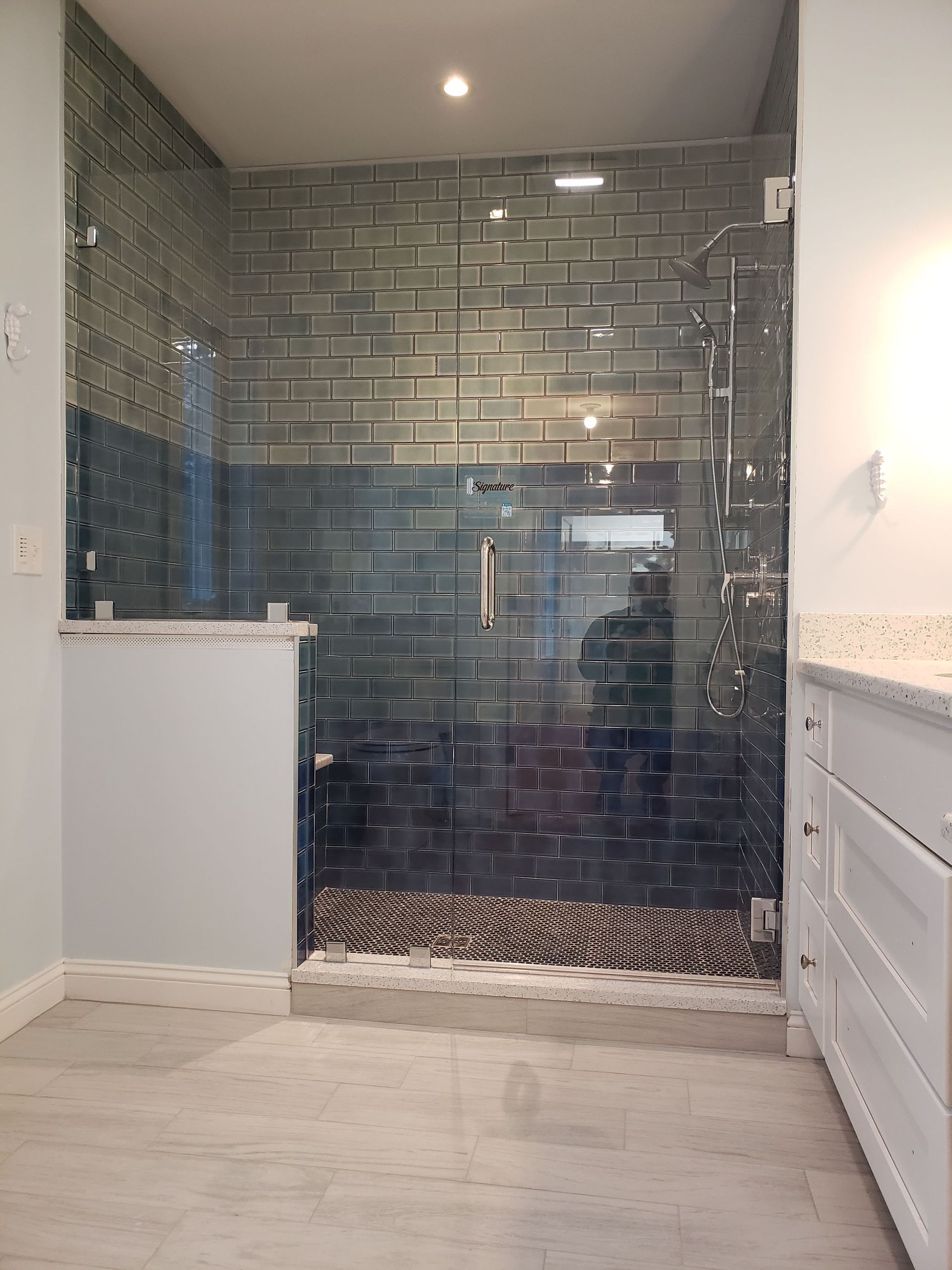 Glass-enclosed shower with blue-green brick-like tiles, white trim, and gray floor.