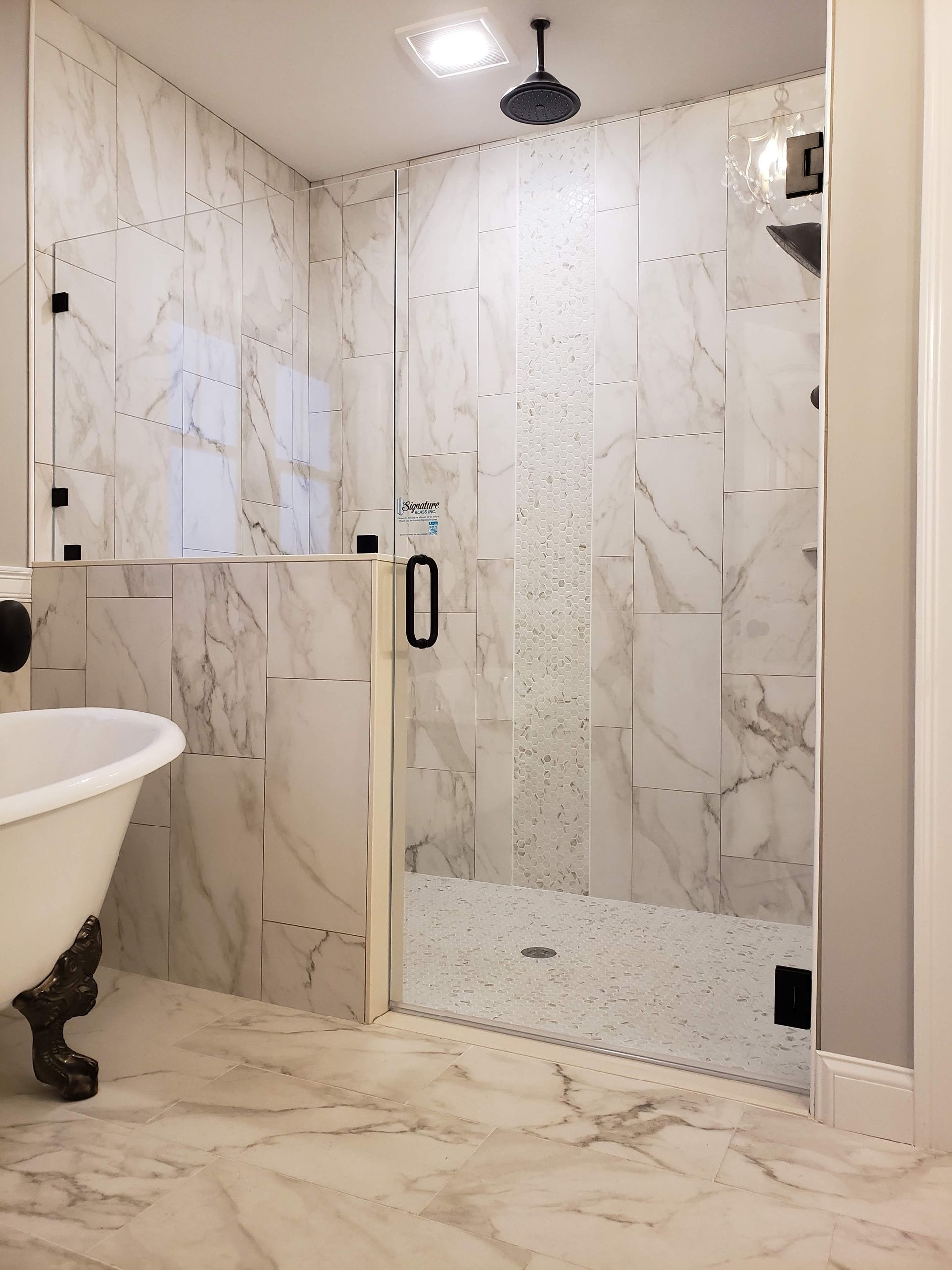 Elegant bathroom with marble tiles, glass shower door, and clawfoot tub.