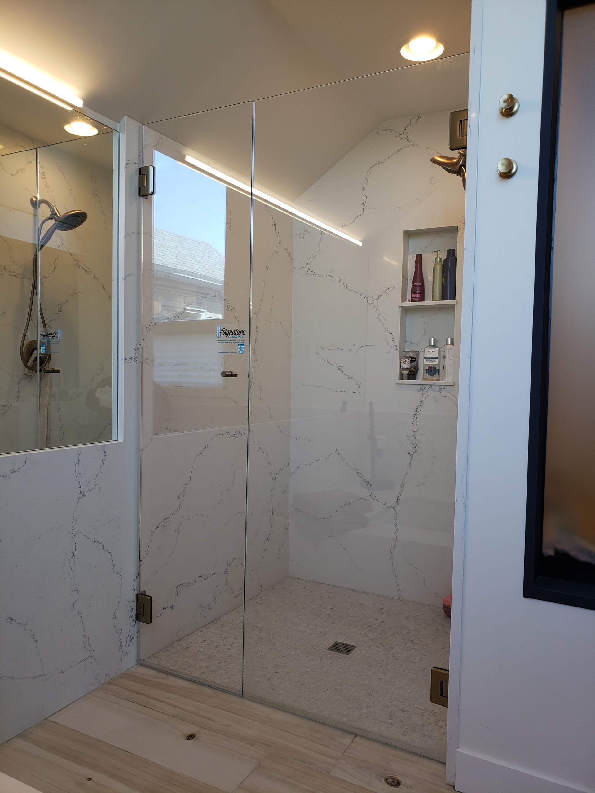 Modern shower with white marble walls, glass door, and pebble floor.