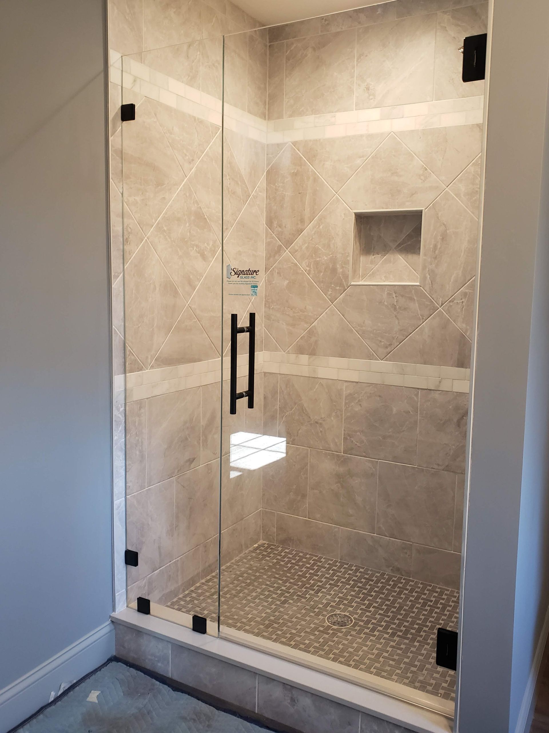 Glass shower enclosure with black hardware and tan tile.