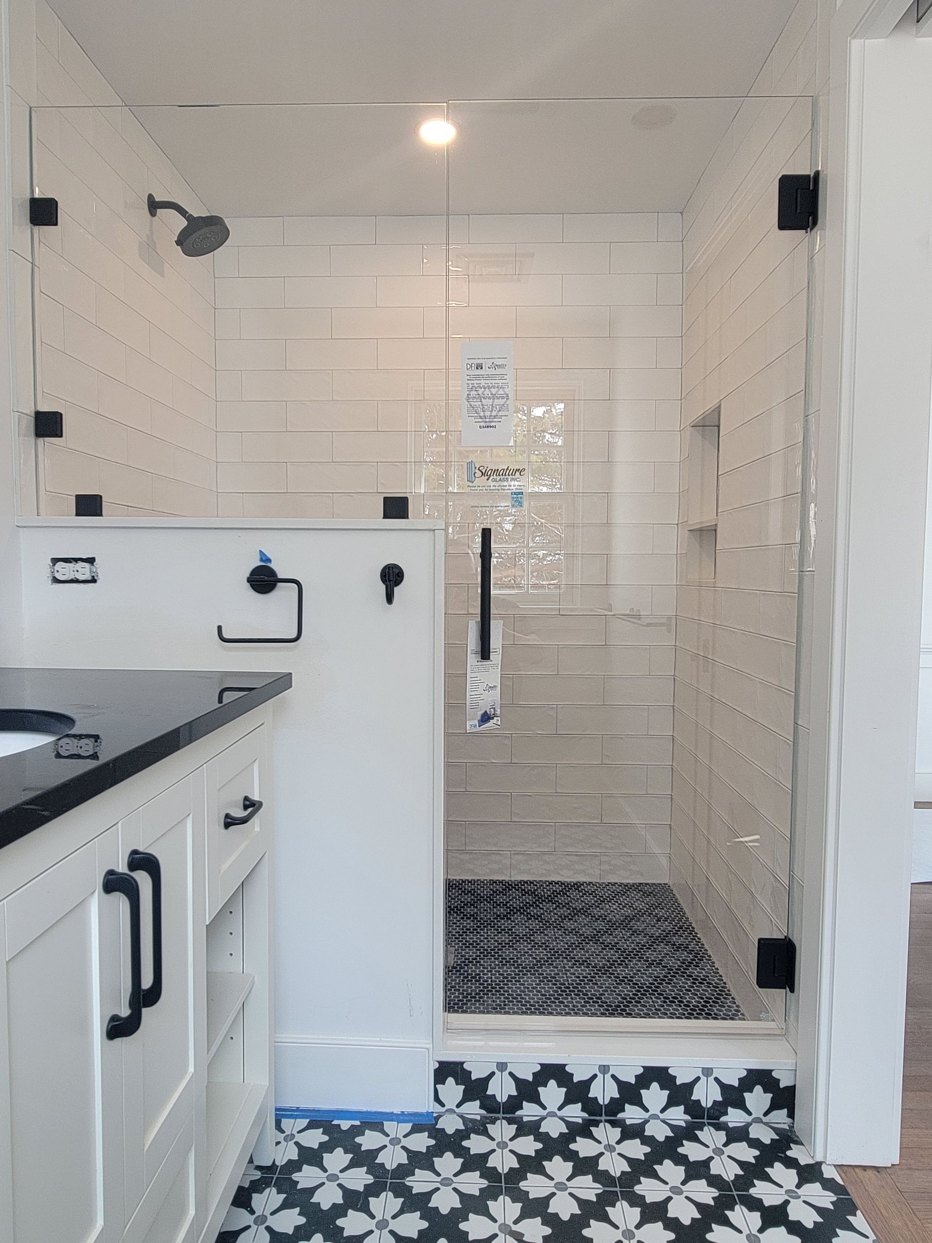 Bathroom with white subway tile shower, black hardware, glass door, and patterned floor tile.