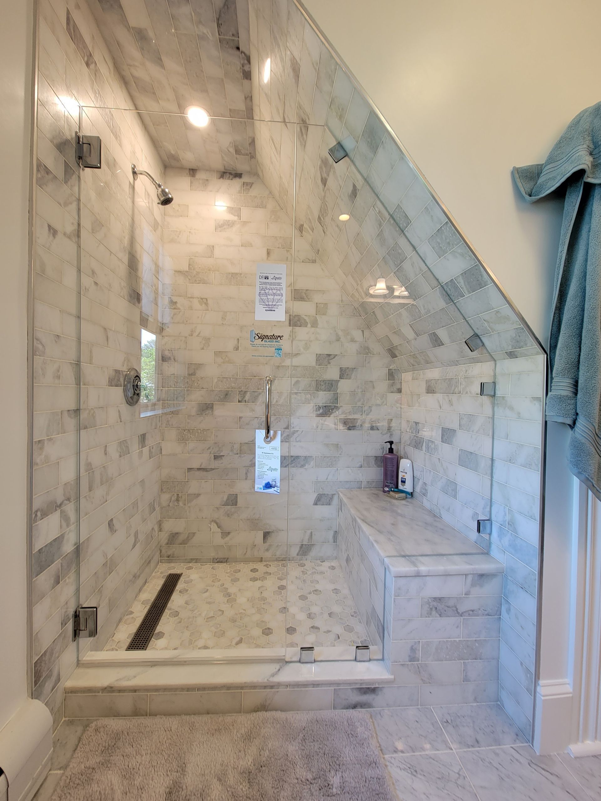 Shower with angled glass door and marble tile. Includes a built-in bench.