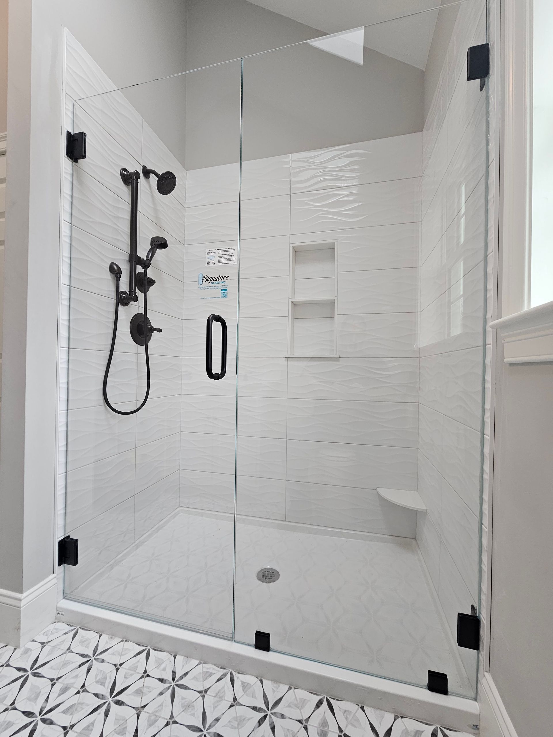 Glass shower with white textured tile walls, black hardware, and a small built-in bench.