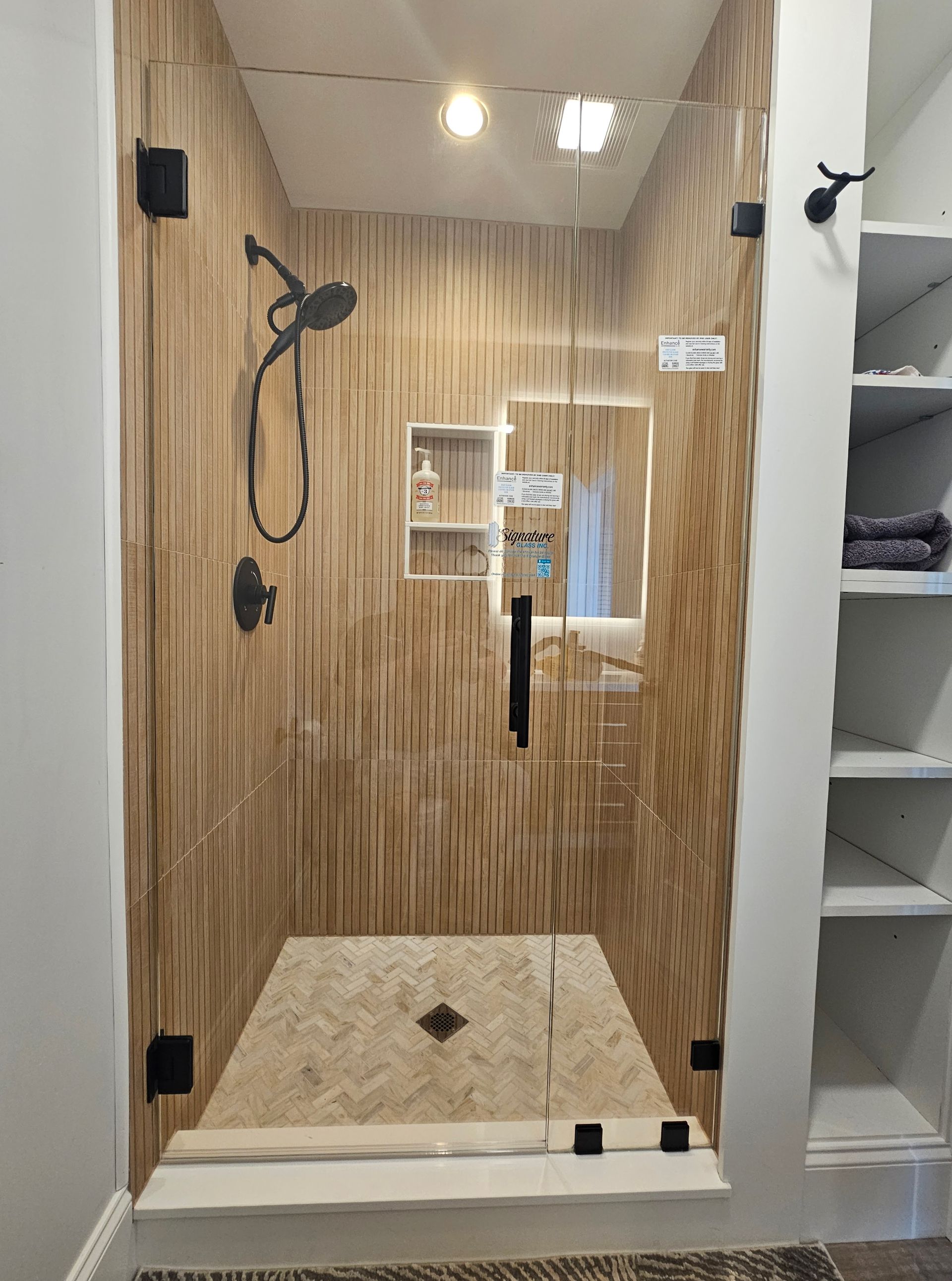 Shower with wood-paneled walls, glass door, black fixtures, and tiled floor.