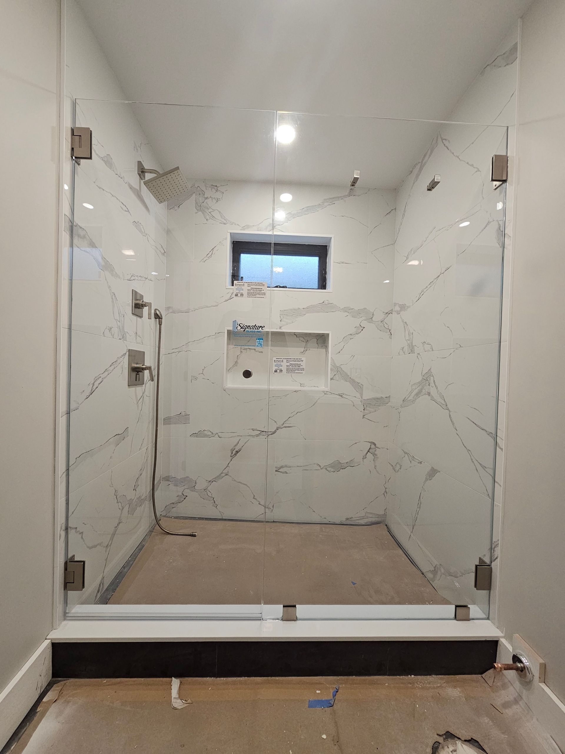 Glass-enclosed shower stall with marble-patterned walls and a small window.