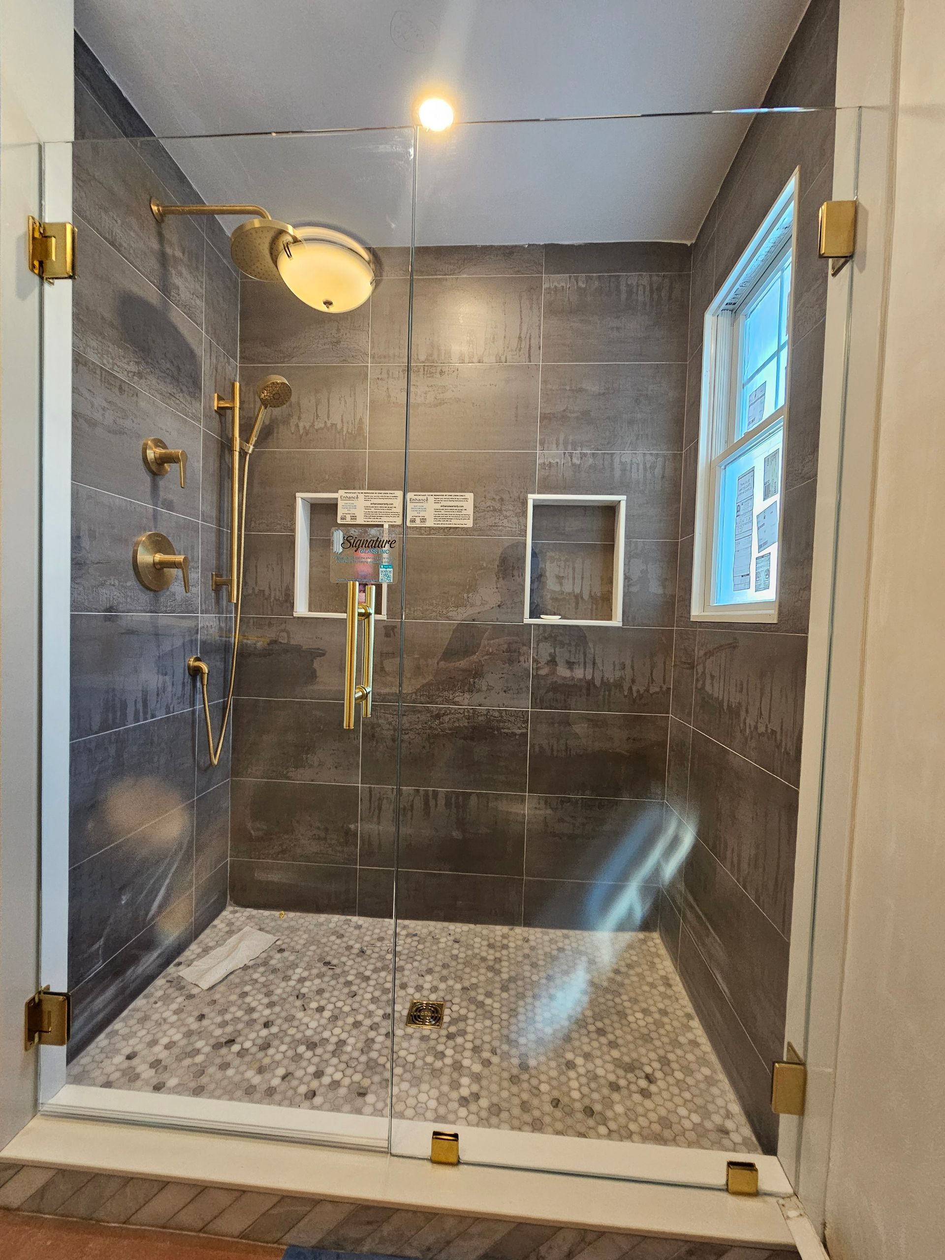 Shower stall with clear glass doors, gold fixtures, and gray tiled walls, pebble floor.