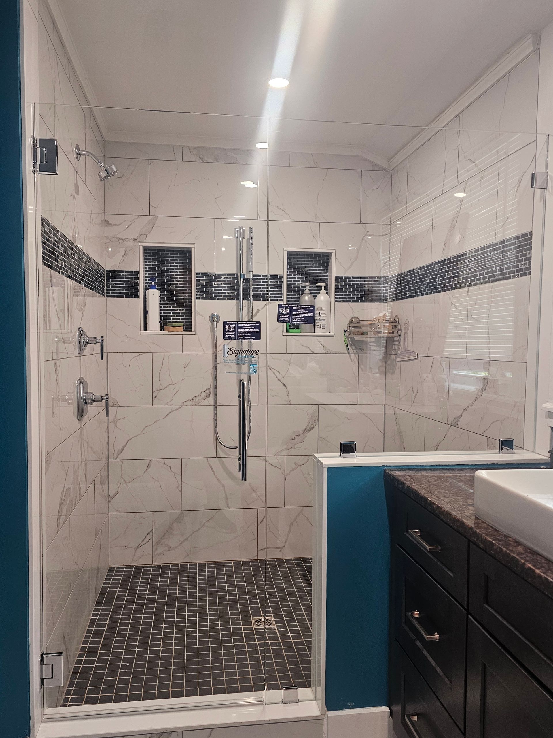 Shower with glass doors, white marble tile, dark blue accent strip, and built-in shelves.