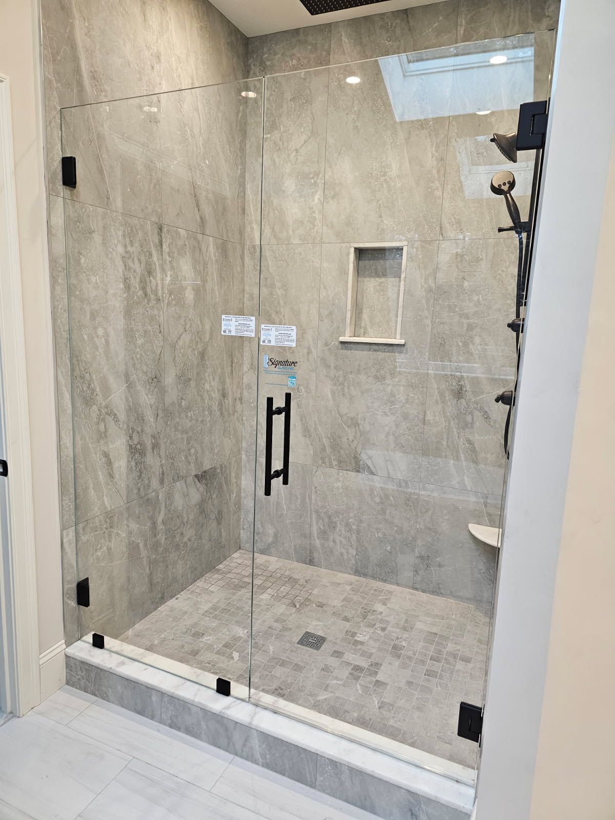 Glass-enclosed shower with black fixtures and gray tile walls and floor. A built-in shelf is visible.