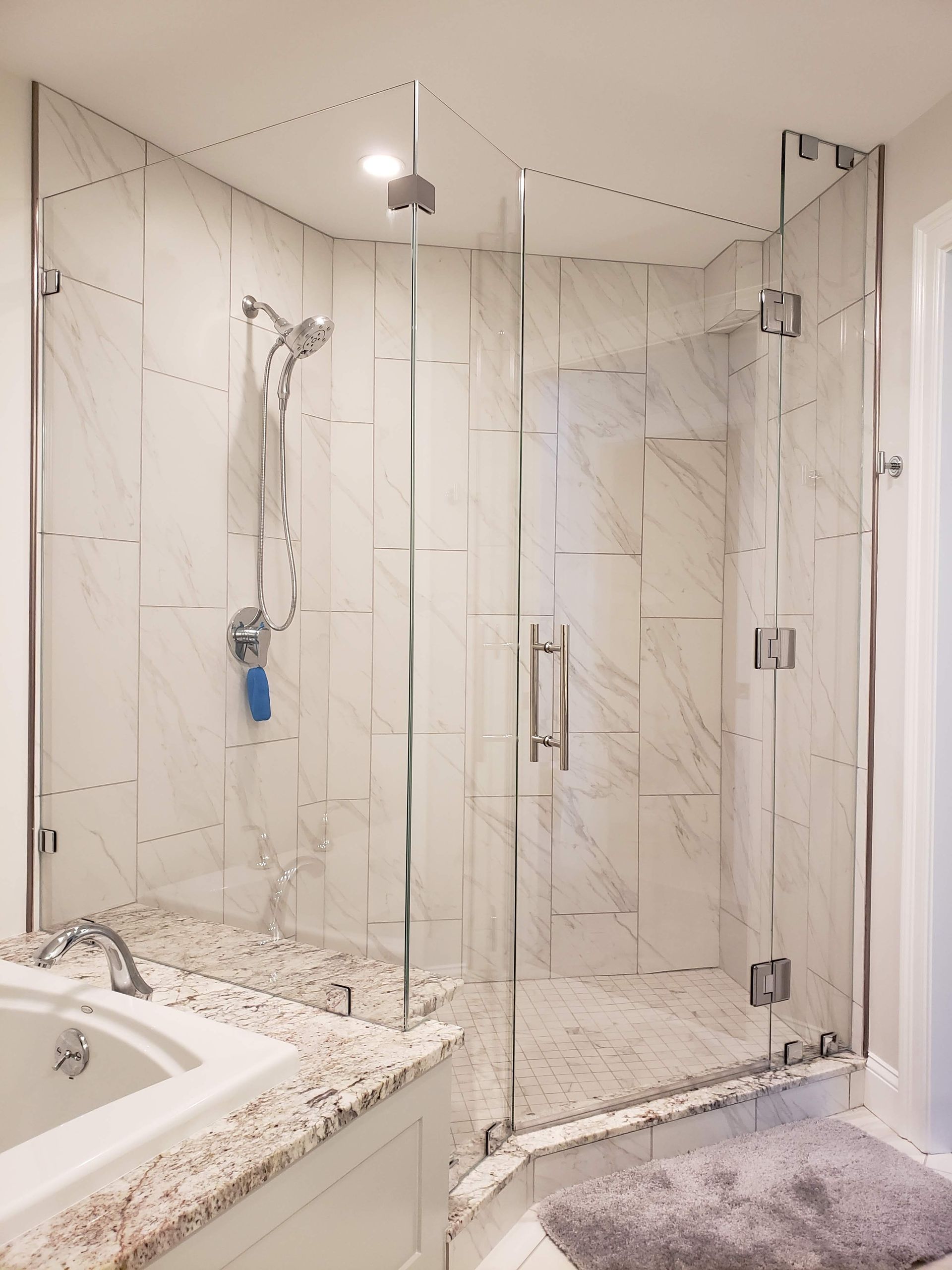 Glass shower enclosure with white tile walls and granite countertop.