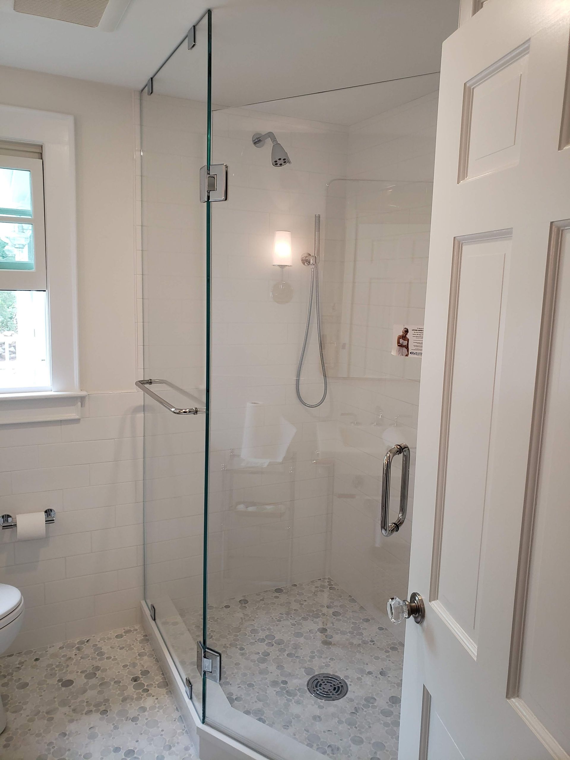 Bathroom with glass shower, white tile, and marble floor.