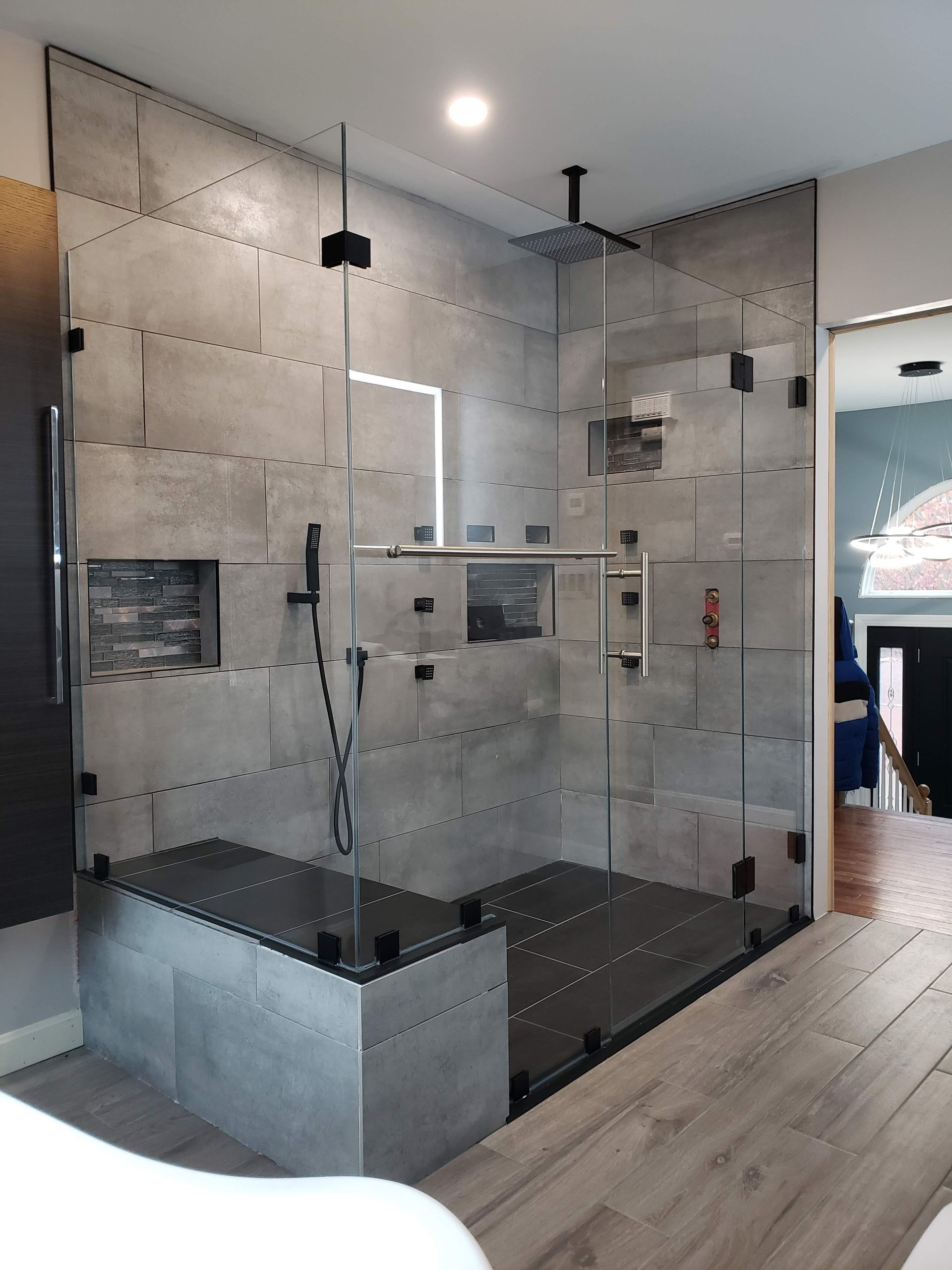 Modern gray tiled shower with glass doors, black fixtures, and a built-in bench.