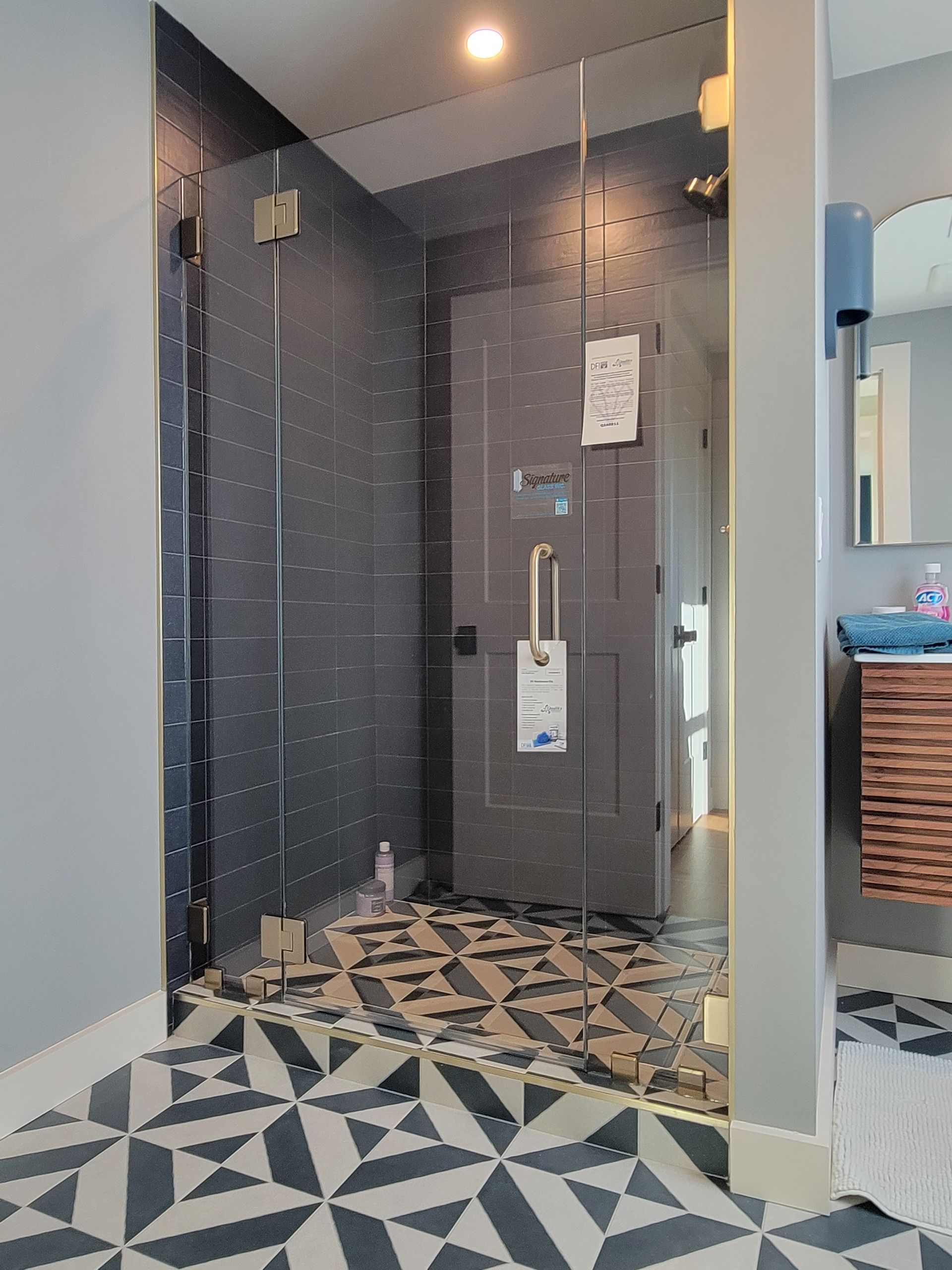 Glass shower door in a bathroom with patterned tile floor, dark blue walls, and a wooden vanity.