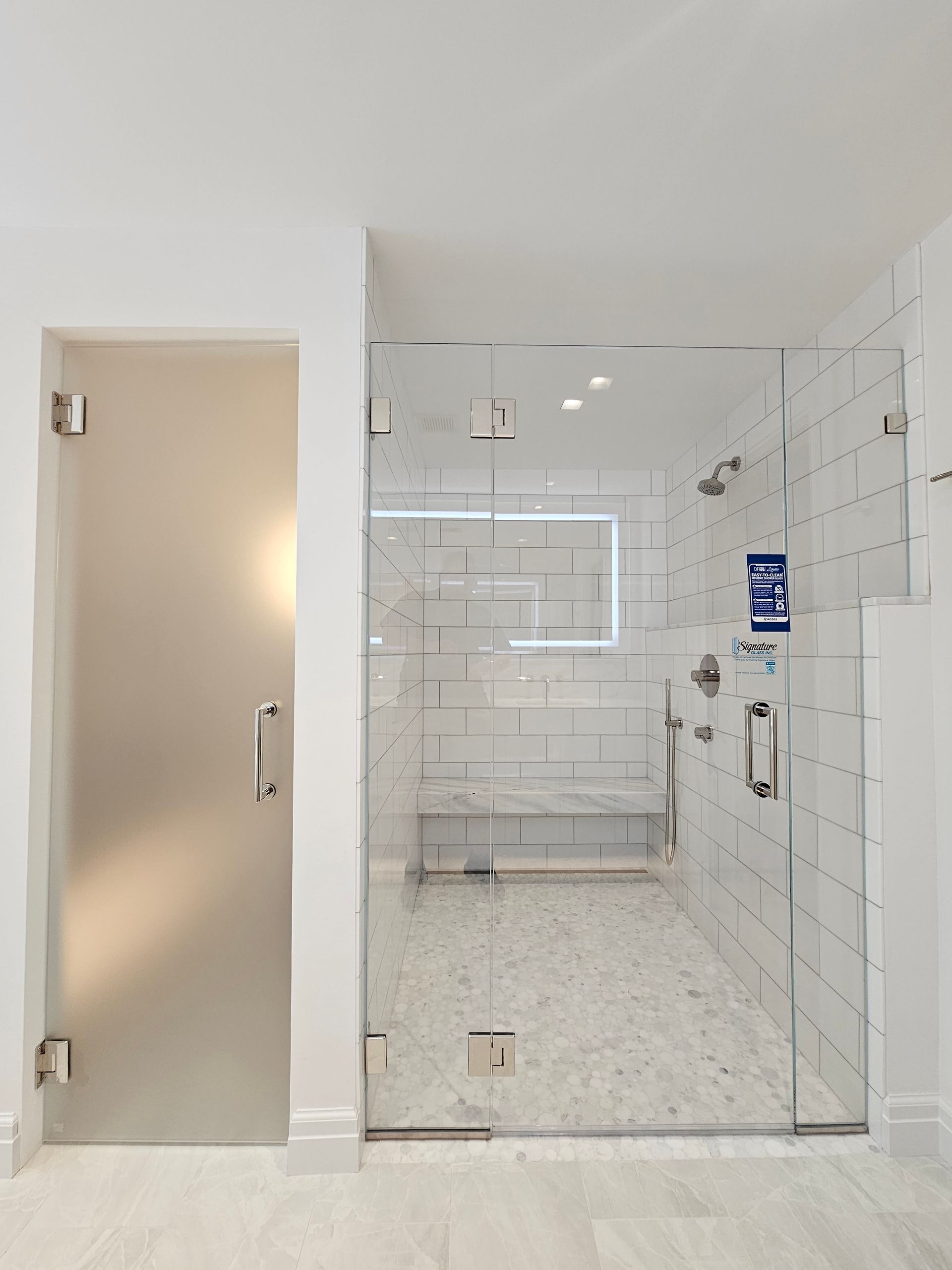 Glass shower with frosted door, white tiled walls and floor, and chrome fixtures.