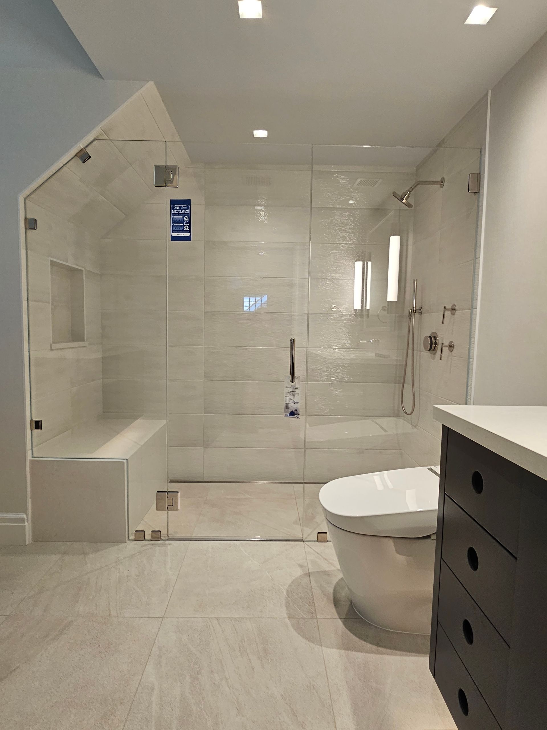Modern bathroom with glass shower enclosure, tiled walls, toilet, and dark cabinet.