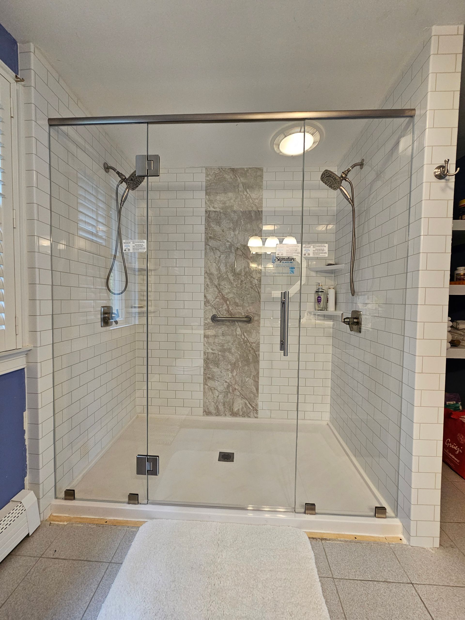 Modern glass-enclosed shower with white tiled walls, silver fixtures, and a light-colored floor.