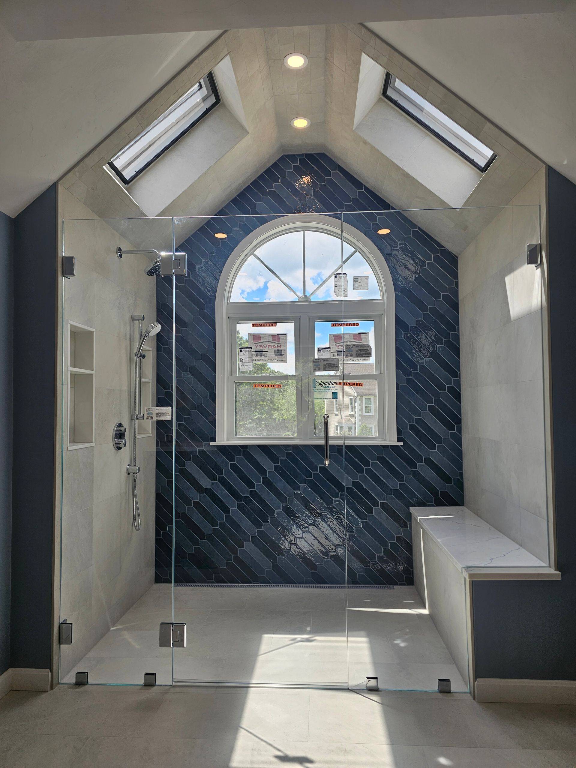 A bathroom with a blue and white tiled shower area, a large window, and skylights.