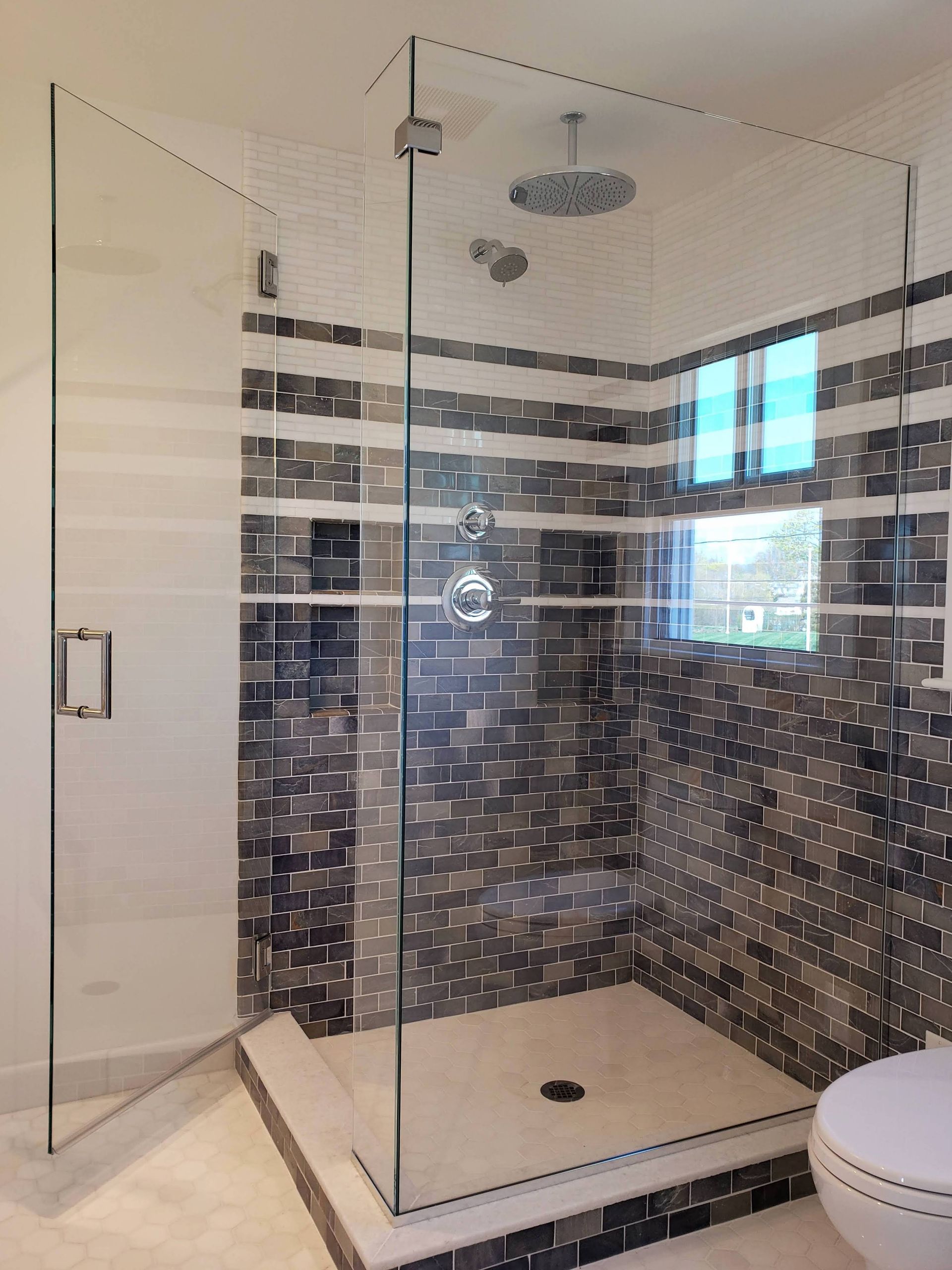 Glass shower enclosure with mosaic tile walls, a rain showerhead, and a white base.