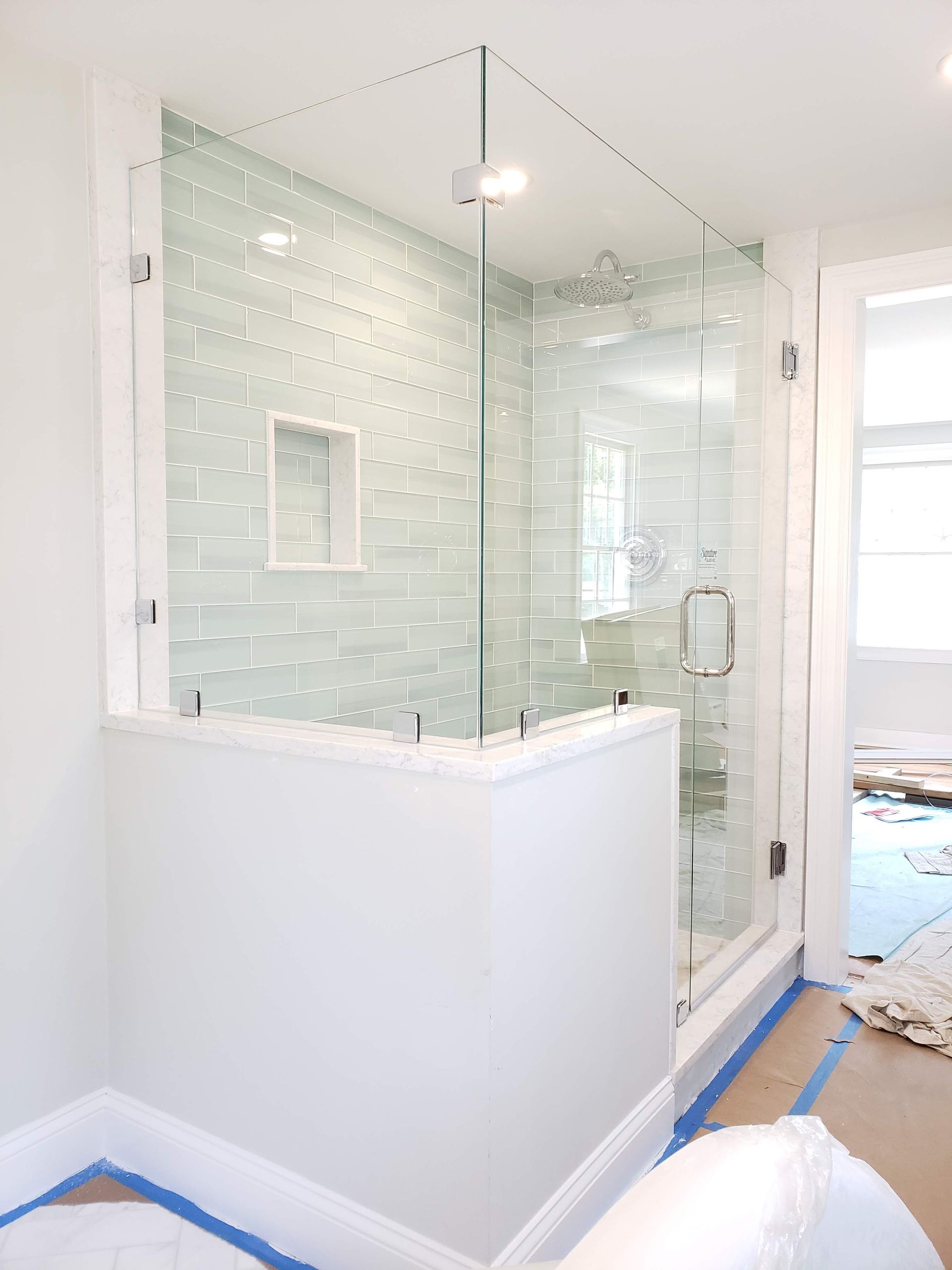 Glass shower enclosure with white walls and light blue textured tile.