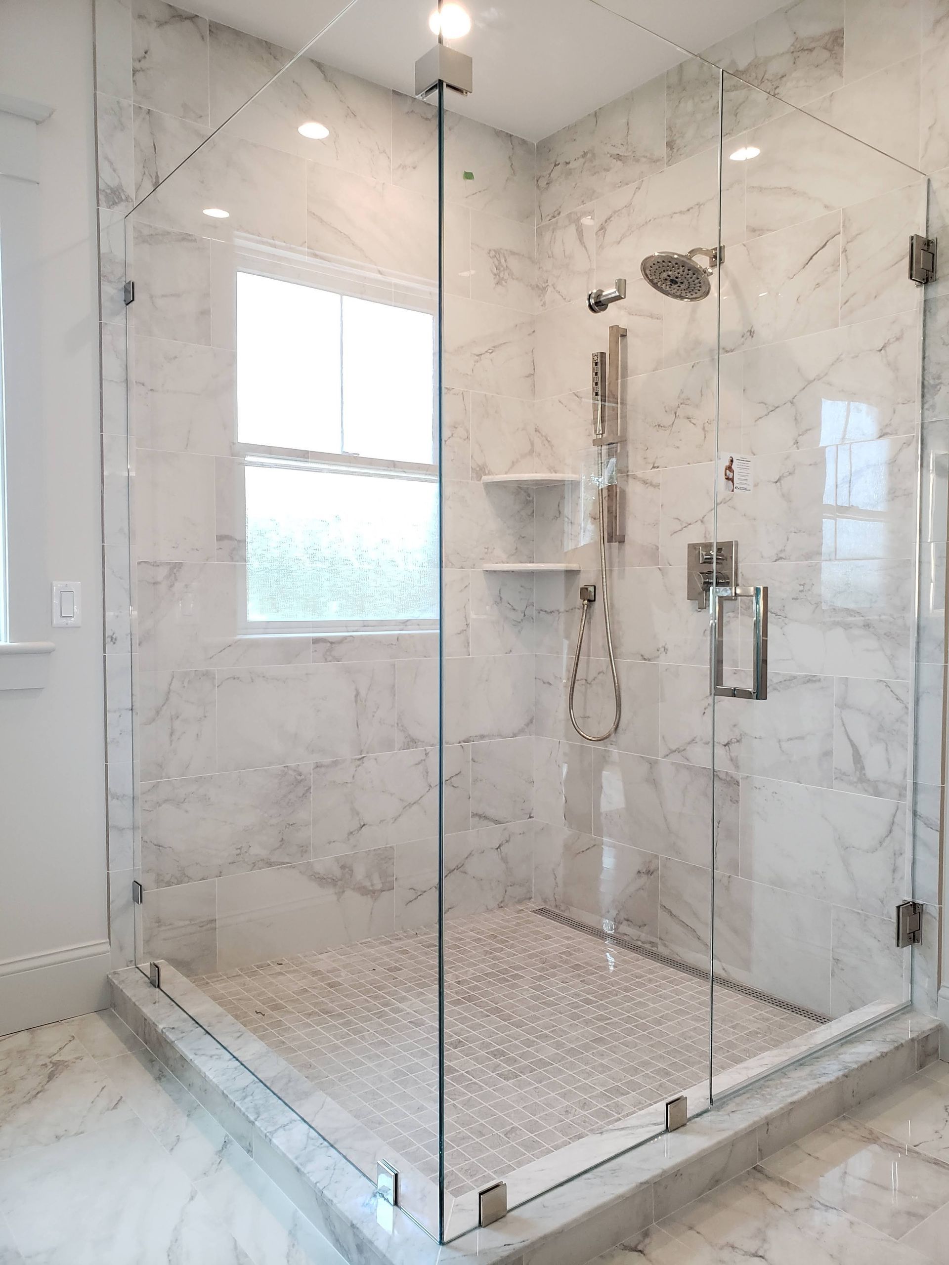 Glass shower with white marble walls and pebble tile floor.