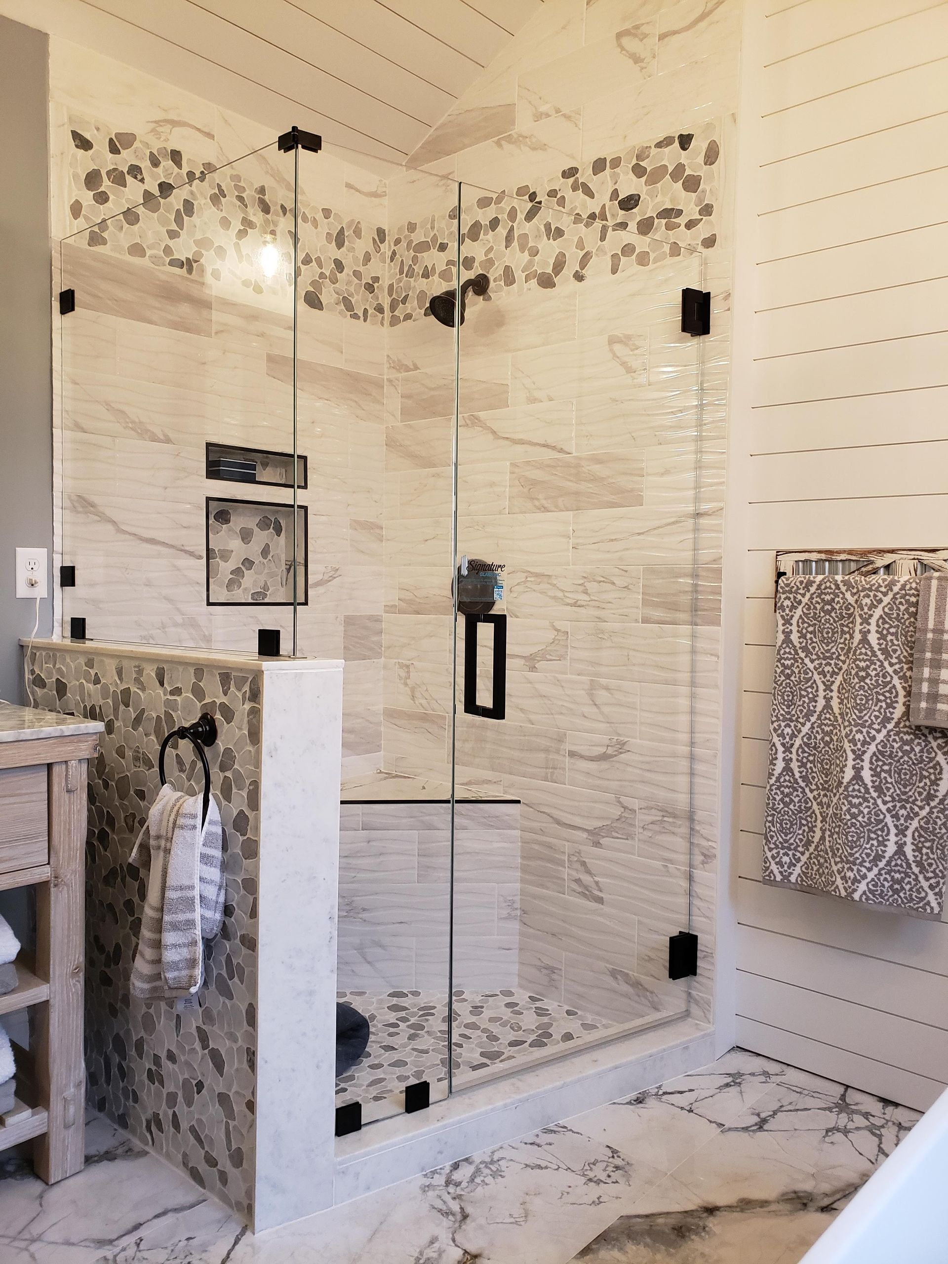 Modern glass shower with black fixtures and decorative tile, next to a sink.