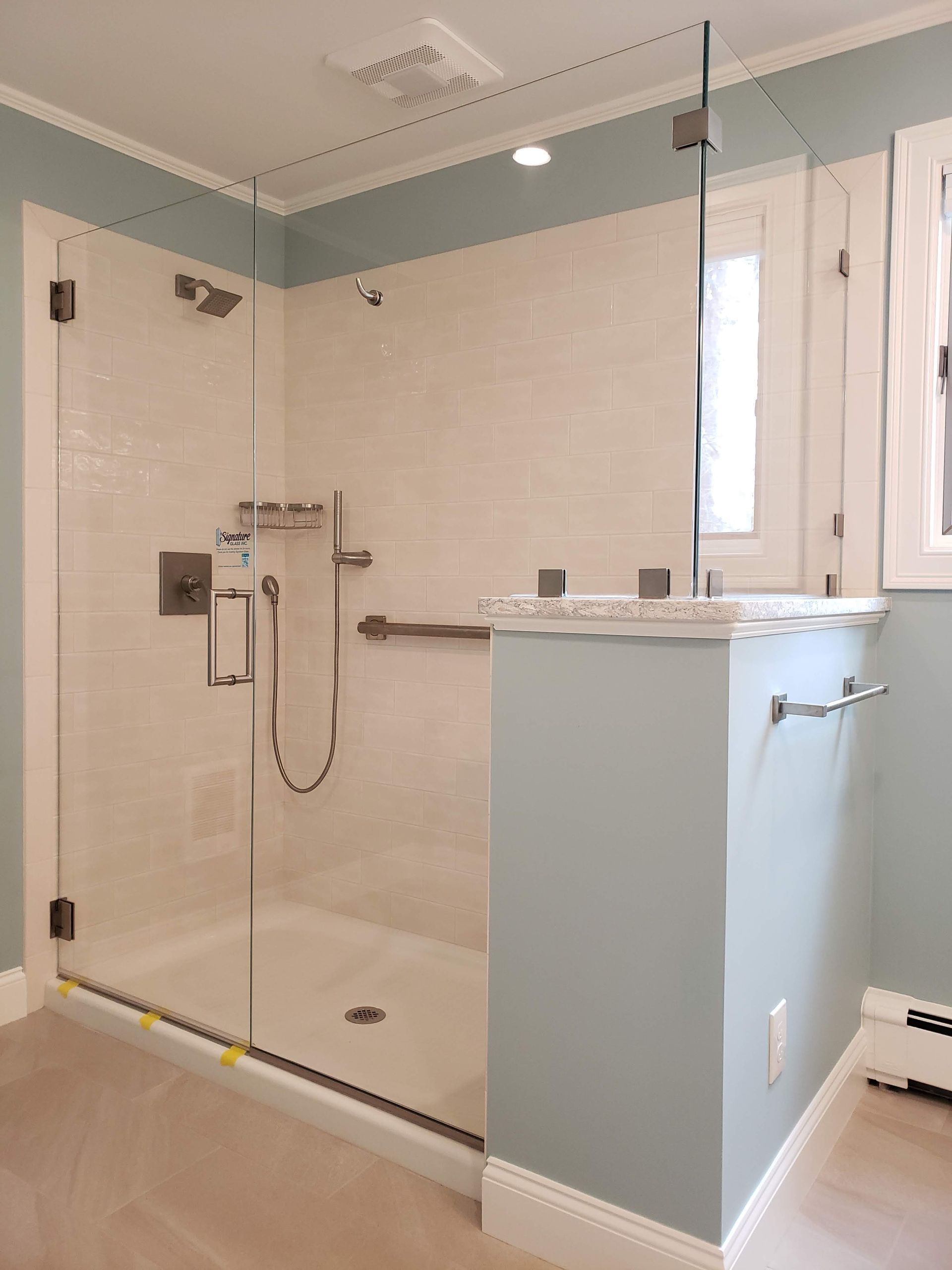 Glass shower enclosure in a bathroom with pale blue walls and white tile.