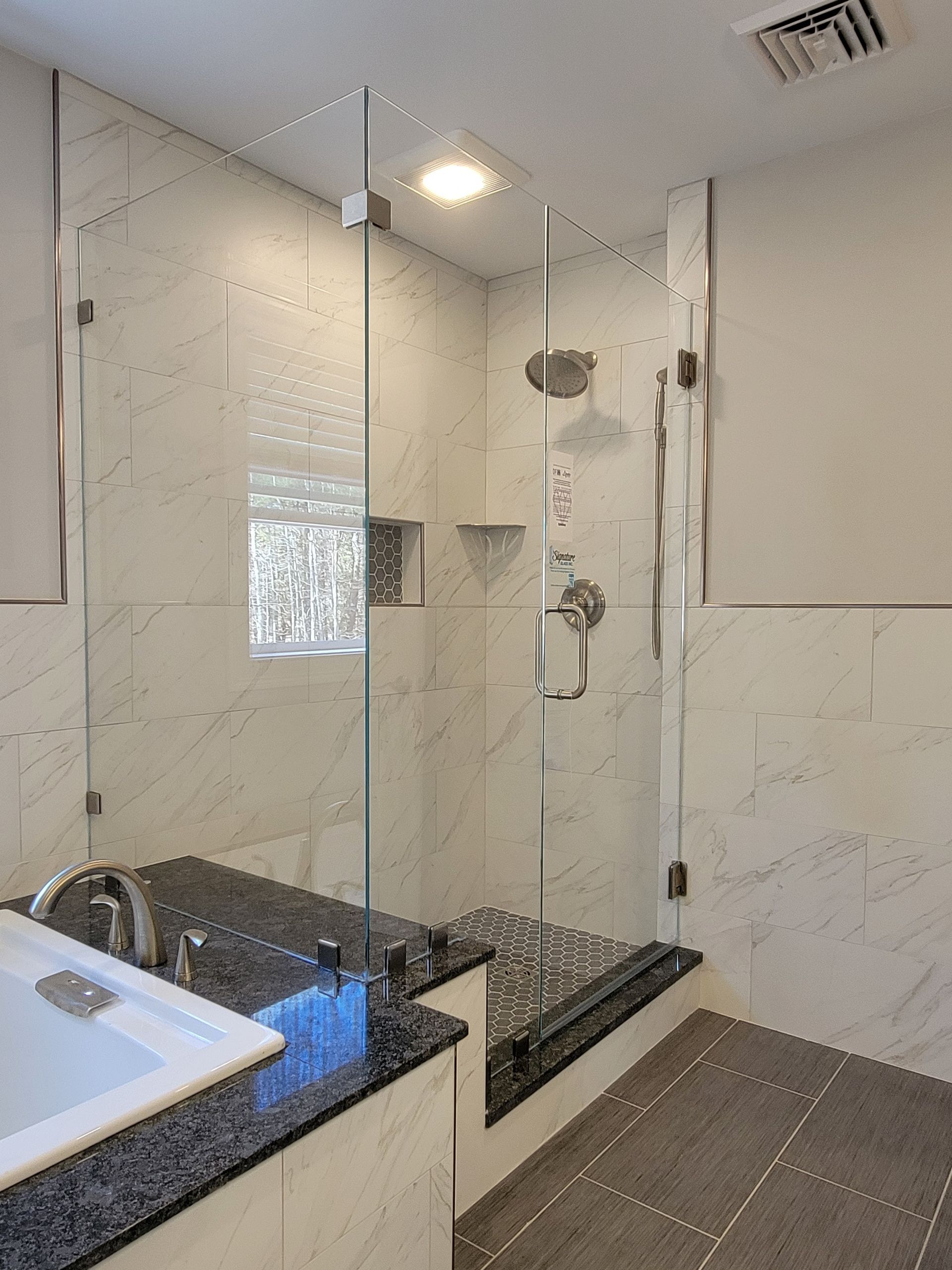 A modern bathroom with a glass shower, marble tile, and a dark granite countertop.