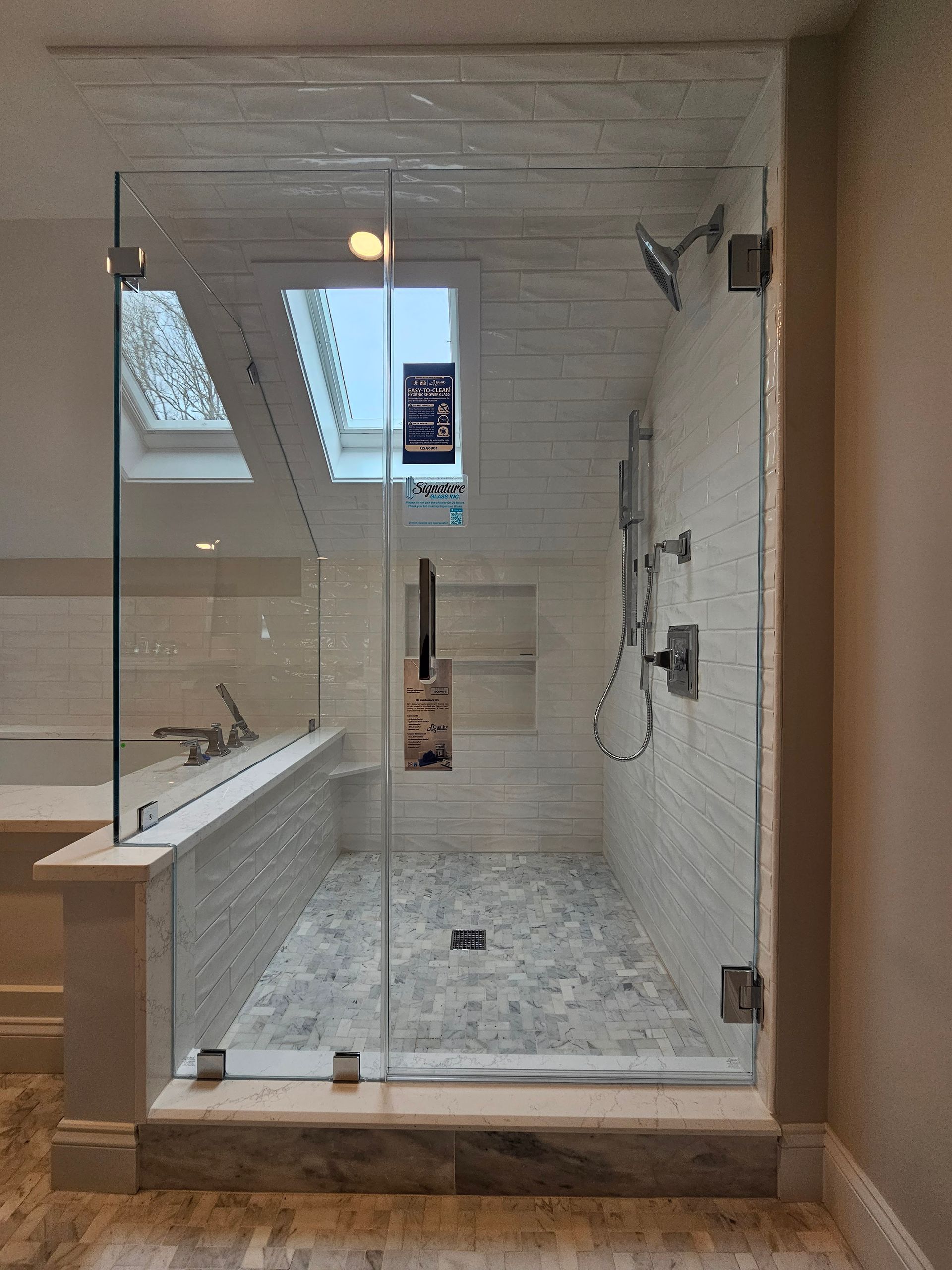 Glass-enclosed shower with pebble floor, white tile walls, and a skylight.