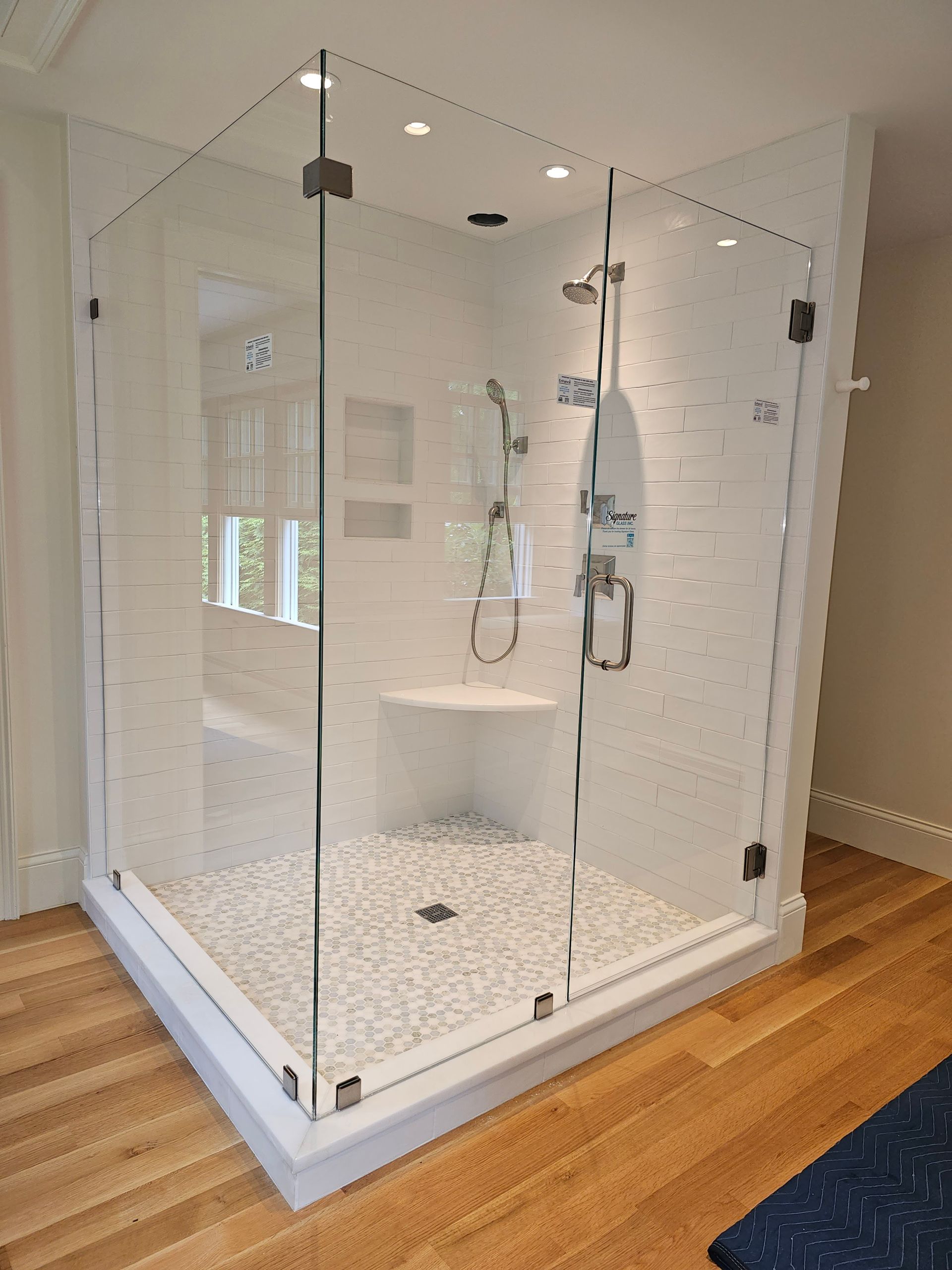 Modern glass shower with white tile walls and pebbled floor, wood flooring.