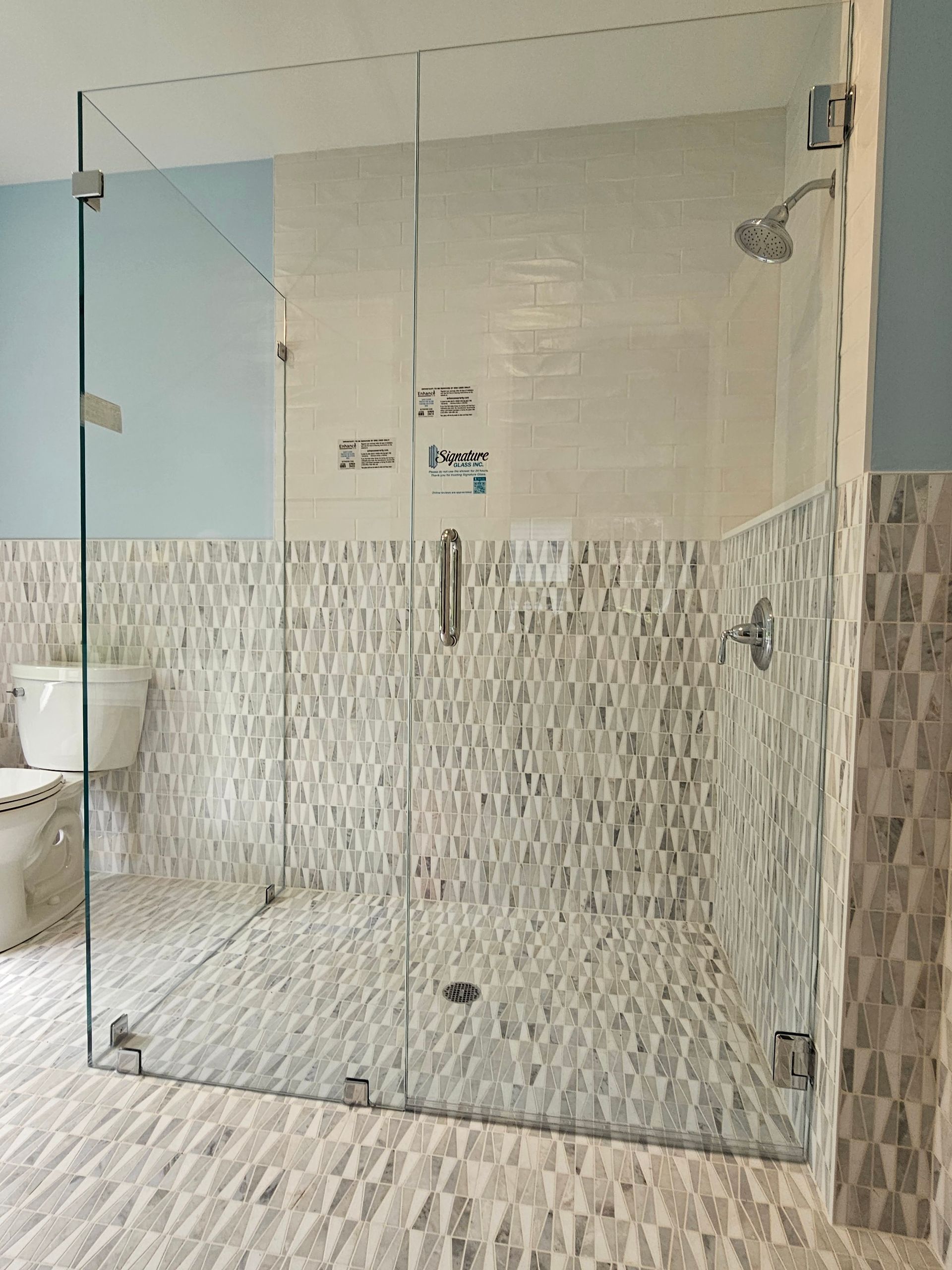 Glass shower enclosure with mosaic tile and light blue walls.