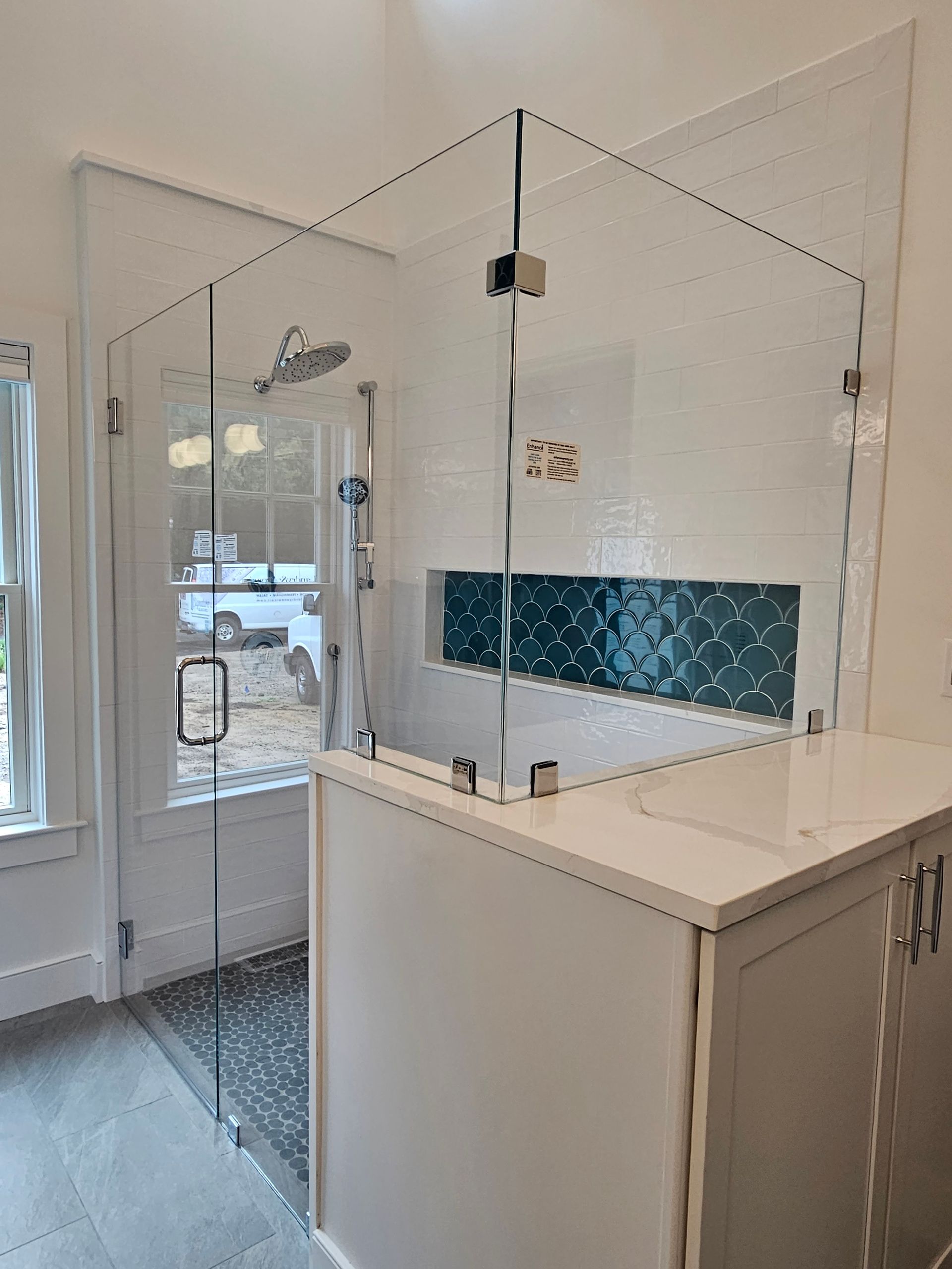 Glass shower enclosure with white cabinets, teal tile, and rain shower head.