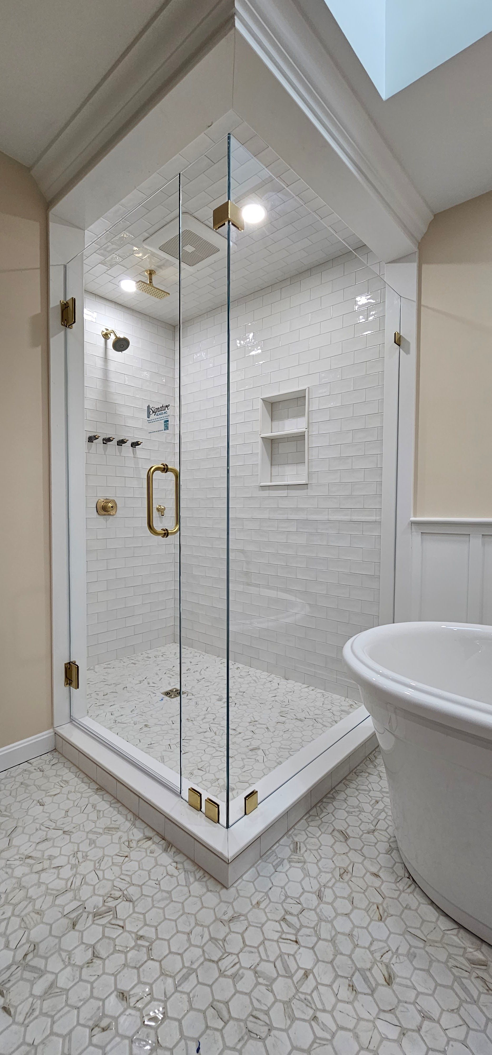 White and gold bathroom with a glass shower and freestanding tub. Hexagon tile covers the floor and shower walls.