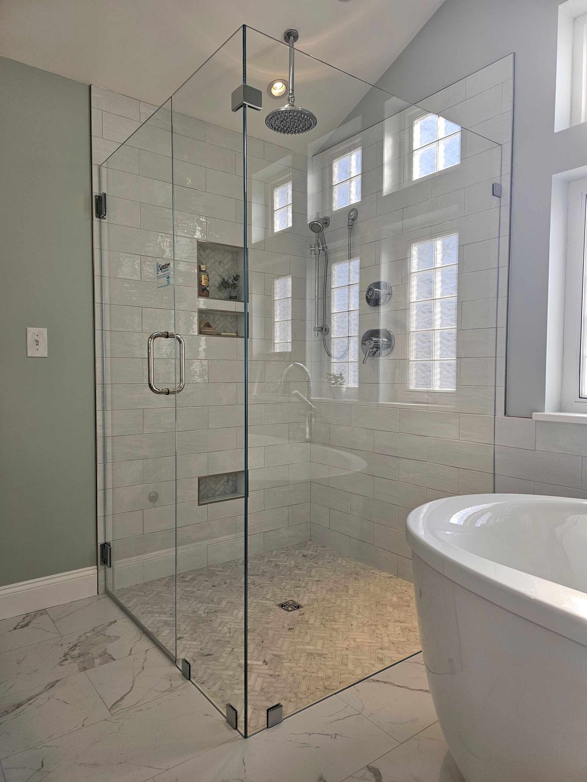 Glass-walled shower with white tile and fixtures, next to a bathtub. Light blue walls.